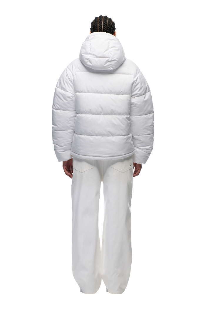 A person with braided hair is seen from behind wearing the 6PM PUFFER JACKET WHITE with an adjustable hood and water-repellent finish, paired with white wide-leg pants against a plain light background.