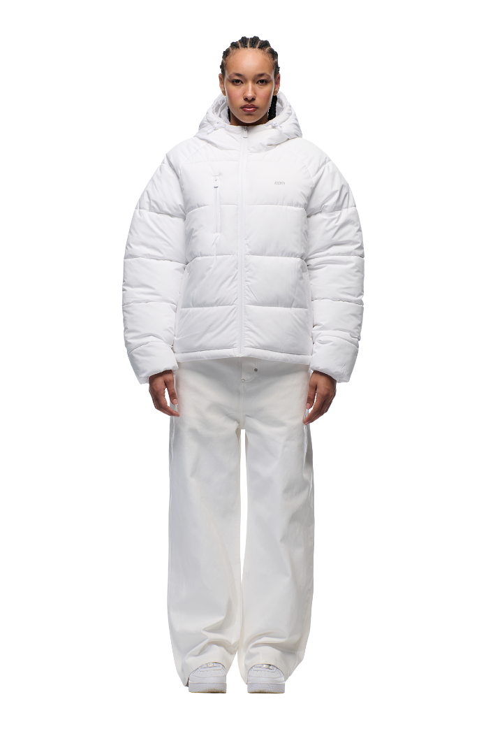 A person faces forward against a plain light background, wearing the 6PM PUFFER JACKET WHITE with an adjustable hood, paired with white wide-leg pants and white sneakers.
