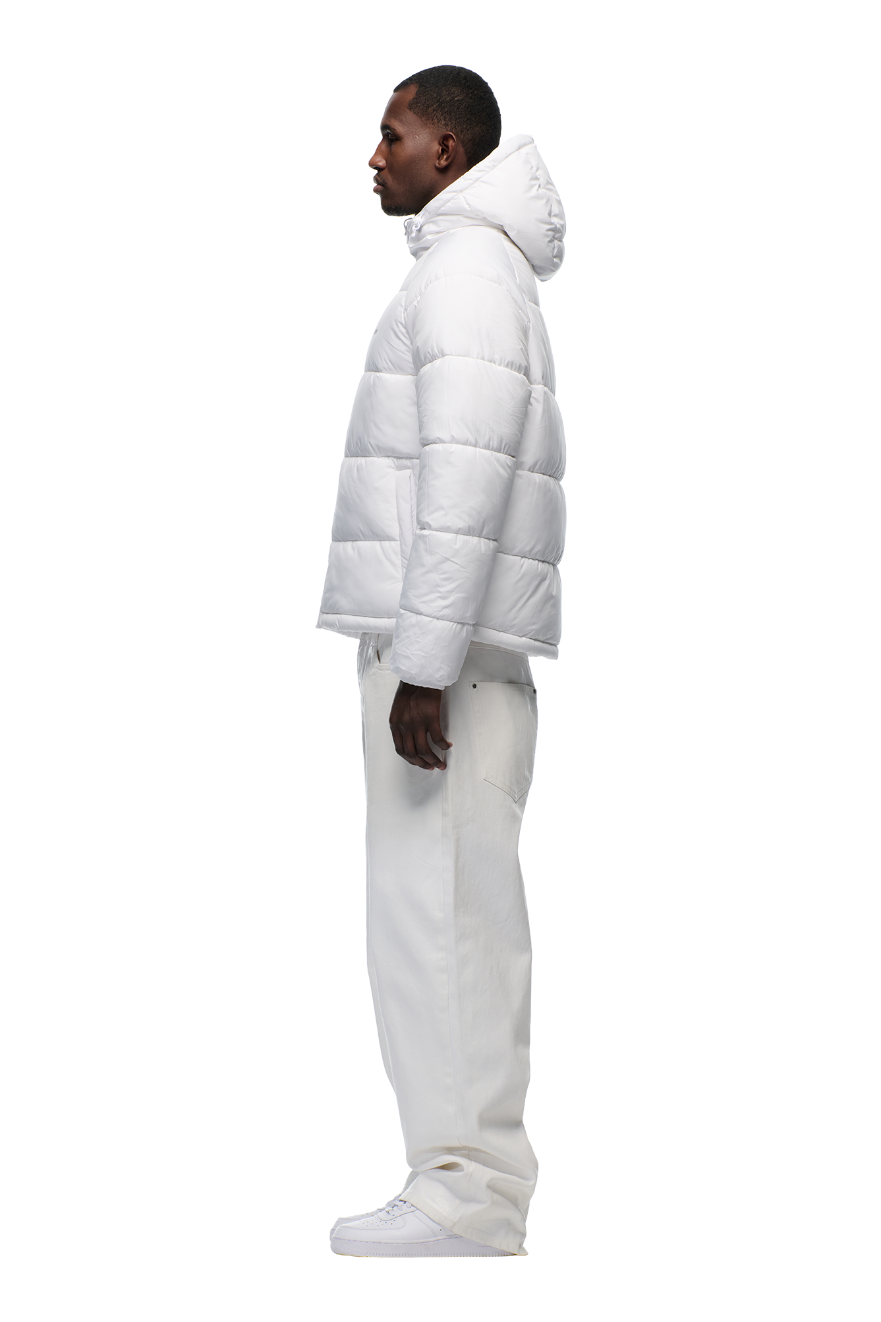 A man stands in profile against a plain white background, wearing the 6PM PUFFER JACKET WHITE with an adjustable hood, paired with white pants and sneakers.