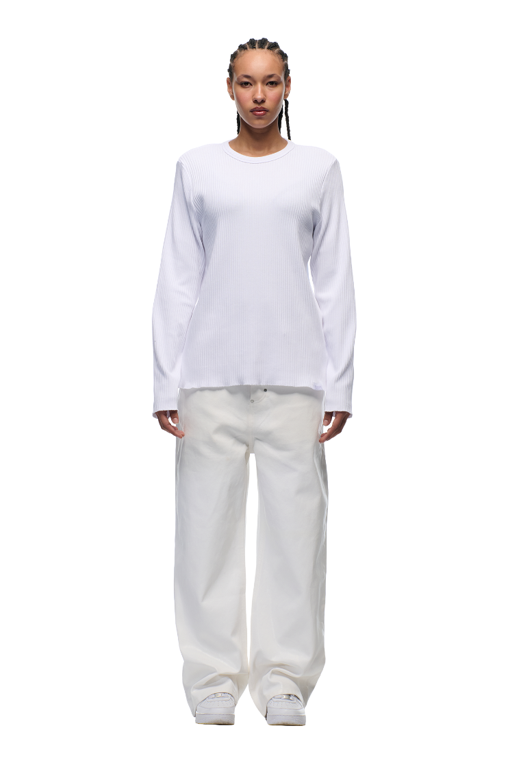 A person stands facing forward against a plain white background, wearing the 6PM+ RIBBED LS WHITE top from 6PM, loose white pants, and white sneakers.