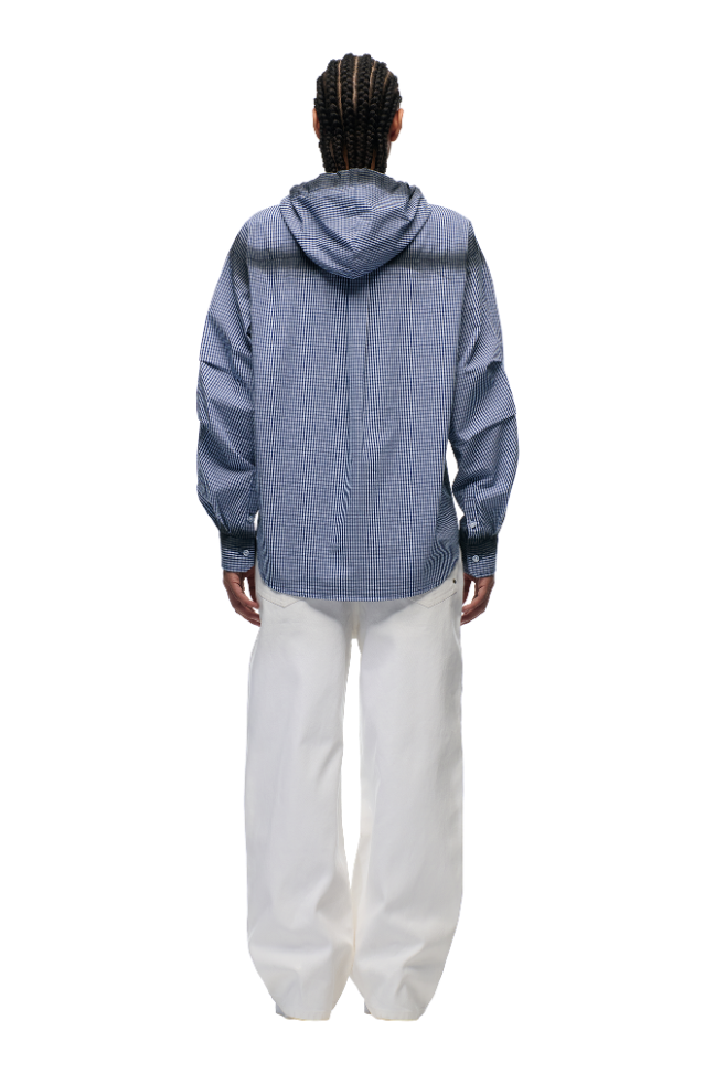 A person with braided hair, facing away from the camera, wears the 6PM HOODED DRESS SHIRT in deep sea blue/white with a patch pocket and adjustable hood, paired with loose white pants, against a plain white background.