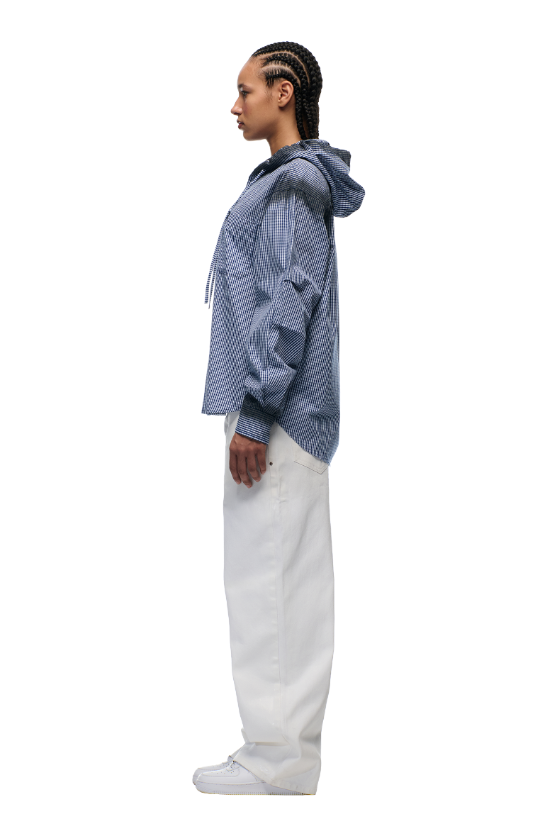 A person with braided hair stands in profile wearing the 6PM HOODED DRESS SHIRT DEEP SEA BLUE/WHITE, paired with loose white pants and white shoes, set against a plain white background.