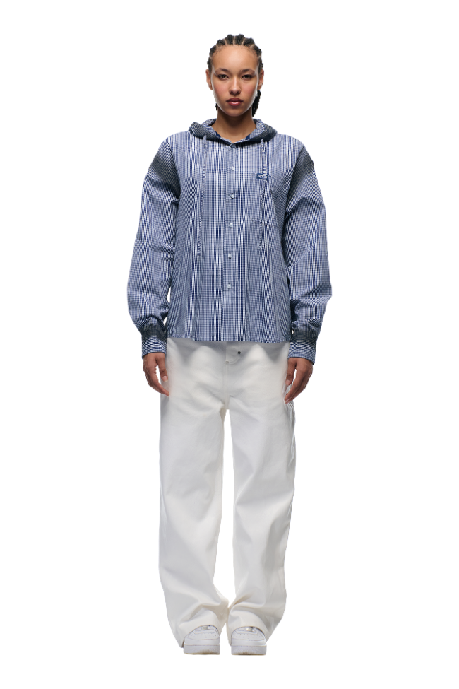 A person faces forward against a plain white background, dressed in the 6PM HOODED DRESS SHIRT DEEP SEA BLUE/WHITE, paired with loose-fitting white pants and white sneakers.