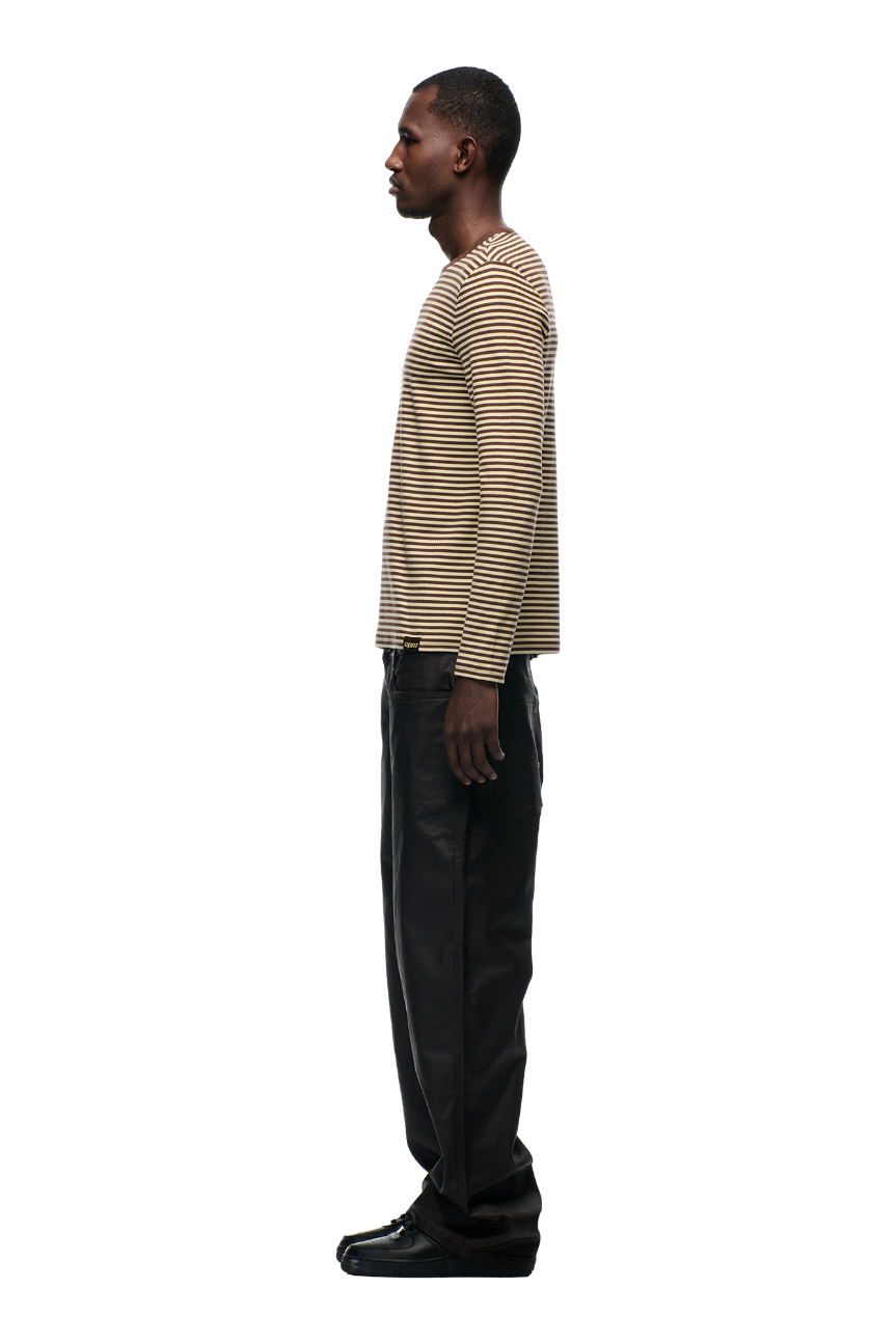 A man stands in profile against a plain background, wearing the 6PM STRIPED RIBBED LS DARK HAZELNUT top with black pants and black shoes.