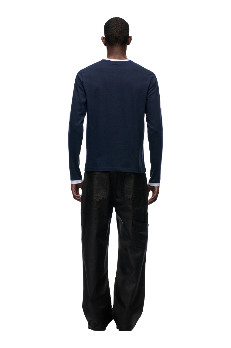 A person stands with their back to the camera, wearing the 6PM GRAFFITI RINGER LS MIDNIGHT BLUE top and loose black pants, set against a plain white background.