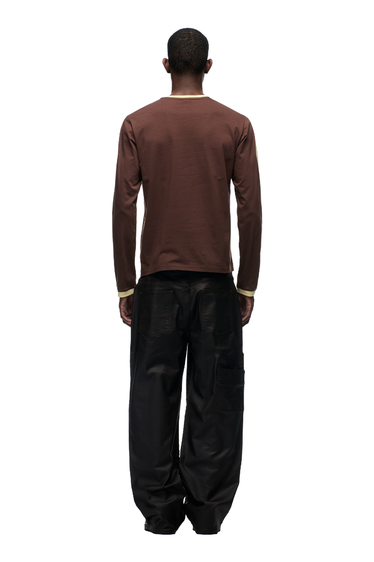 A person faces away from the camera, wearing the 6PM GRAFFITI RINGER LS DARK HAZELNUT top and loose black cargo pants with an embroidered graffiti logo, all set against a plain white background.