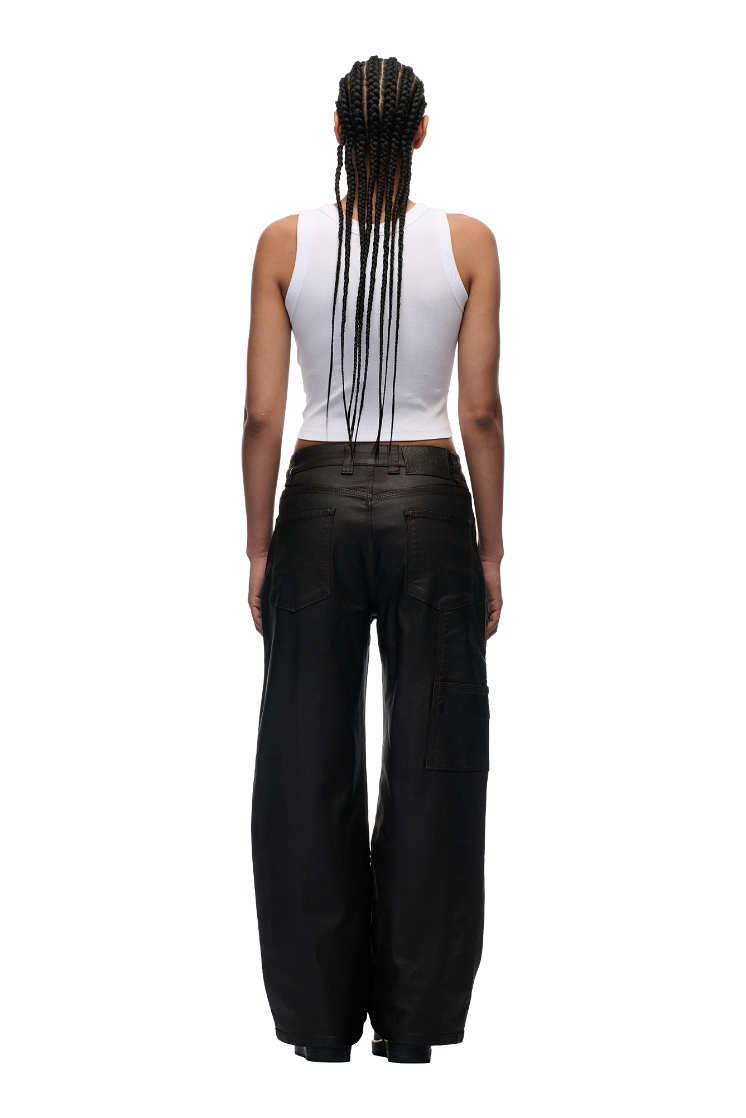 A person with long, braided hair is seen from the back, wearing a white sleeveless crop top and 6PM's COATED CARPENTER DENIM HASH BROWNIE pants against a plain white background.