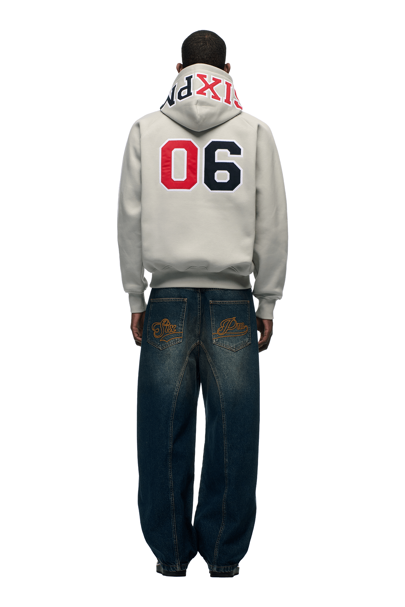 A person faces away in the 6PM COLLEGE LETTER HOODIE SMOKE GREY, featuring "06" and bold "6PM" on the hood, paired with loose-fit blue jeans with gold back embroidery, set against a plain white background.
