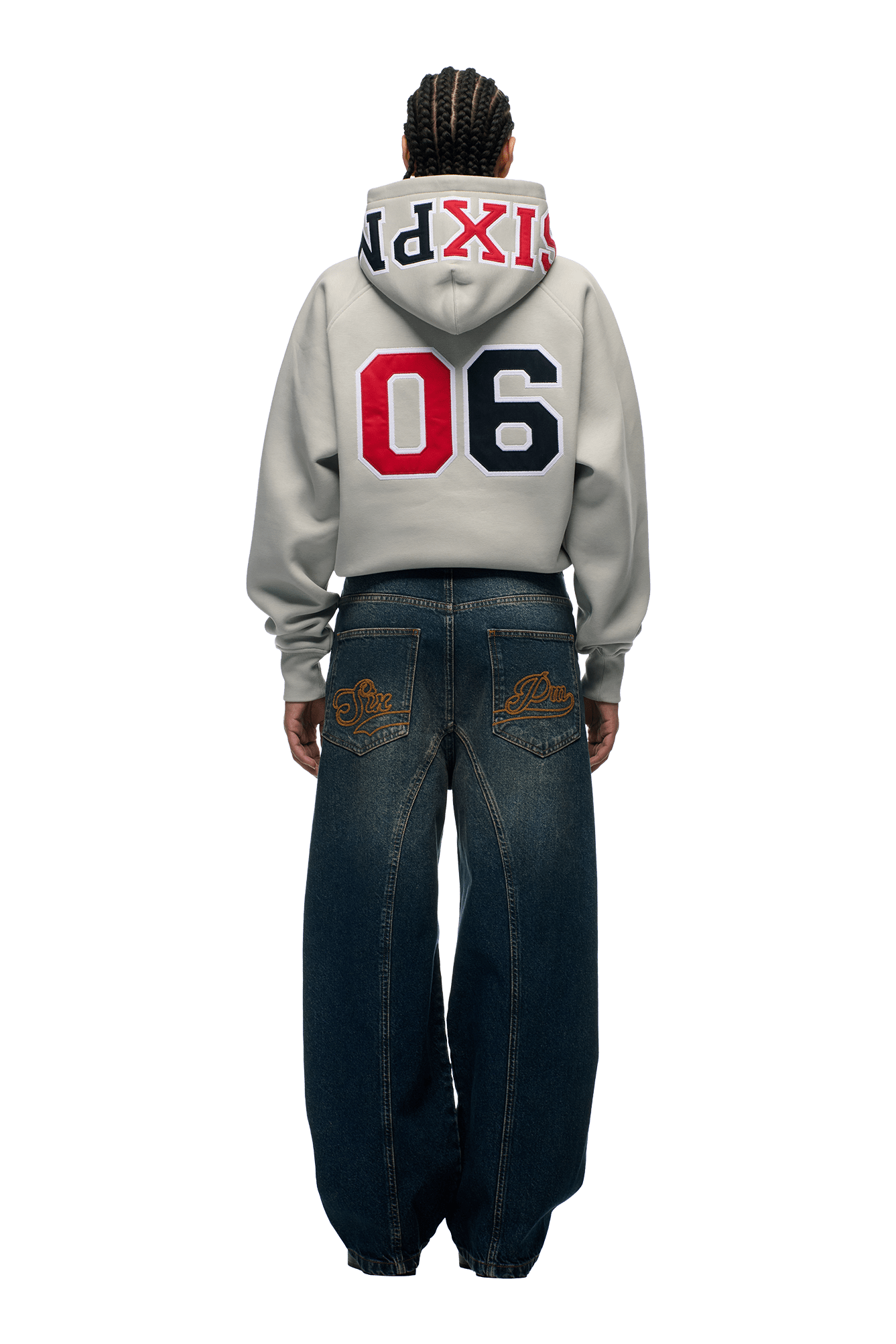A person faces away from the camera in a 6PM COLLEGE LETTER HOODIE SMOKE GREY, featuring red, navy, and white branding, paired with loose dark blue jeans with embroidered back pockets.