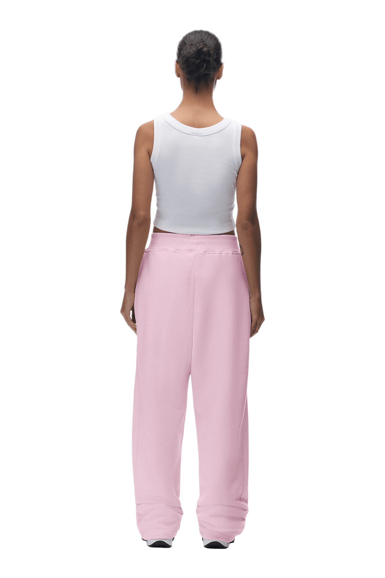 A person stands facing away, wearing the 6PM OPEN LEG JOGGER BABY PINK pants and a sleeveless white top. Their hair is tied back, set against a plain, transparent background.