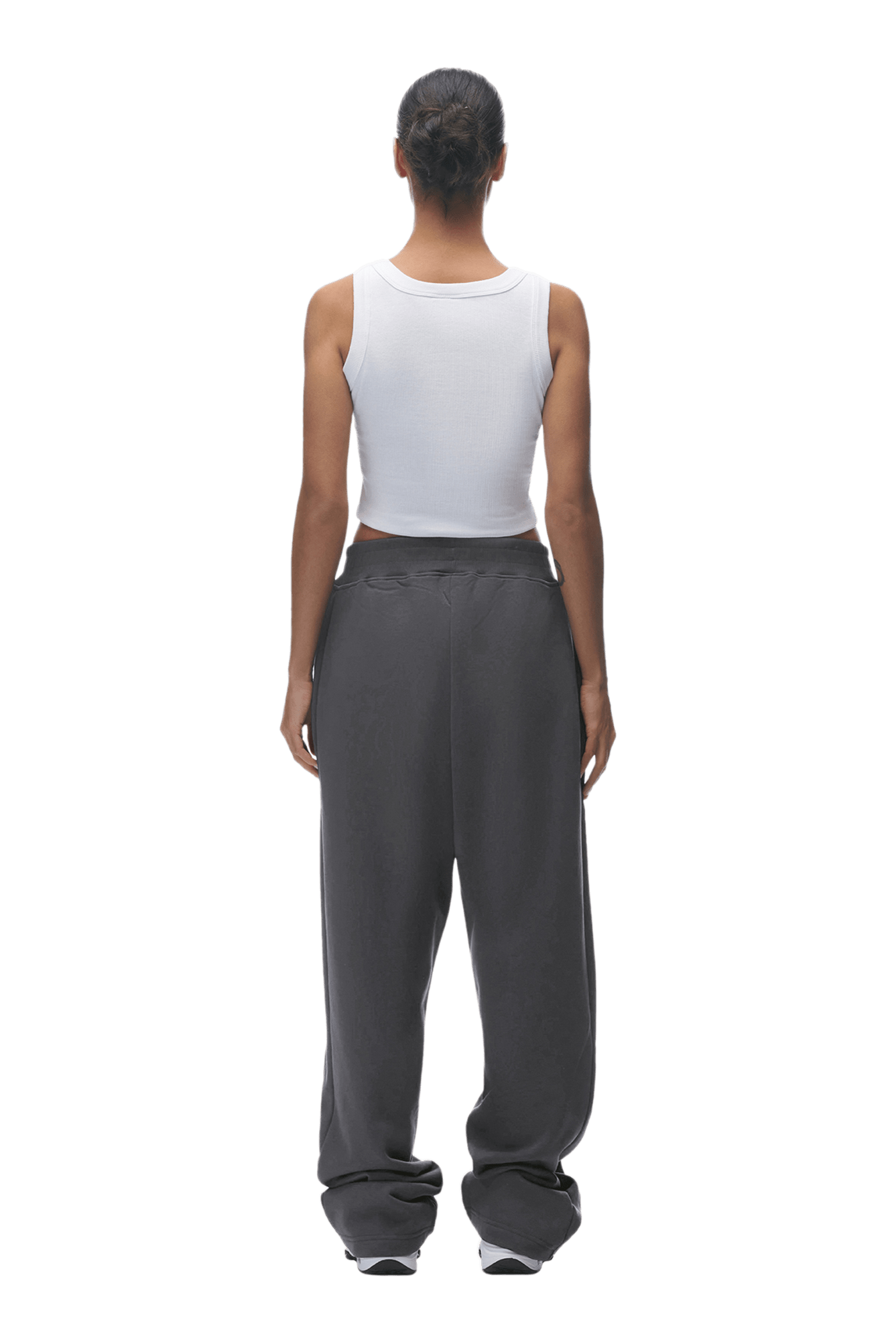 A person stands facing away with hair tied back, wearing a white sleeveless top and 6PM OPEN LEG JOGGER ANTHRACITE pants. The background is transparent.