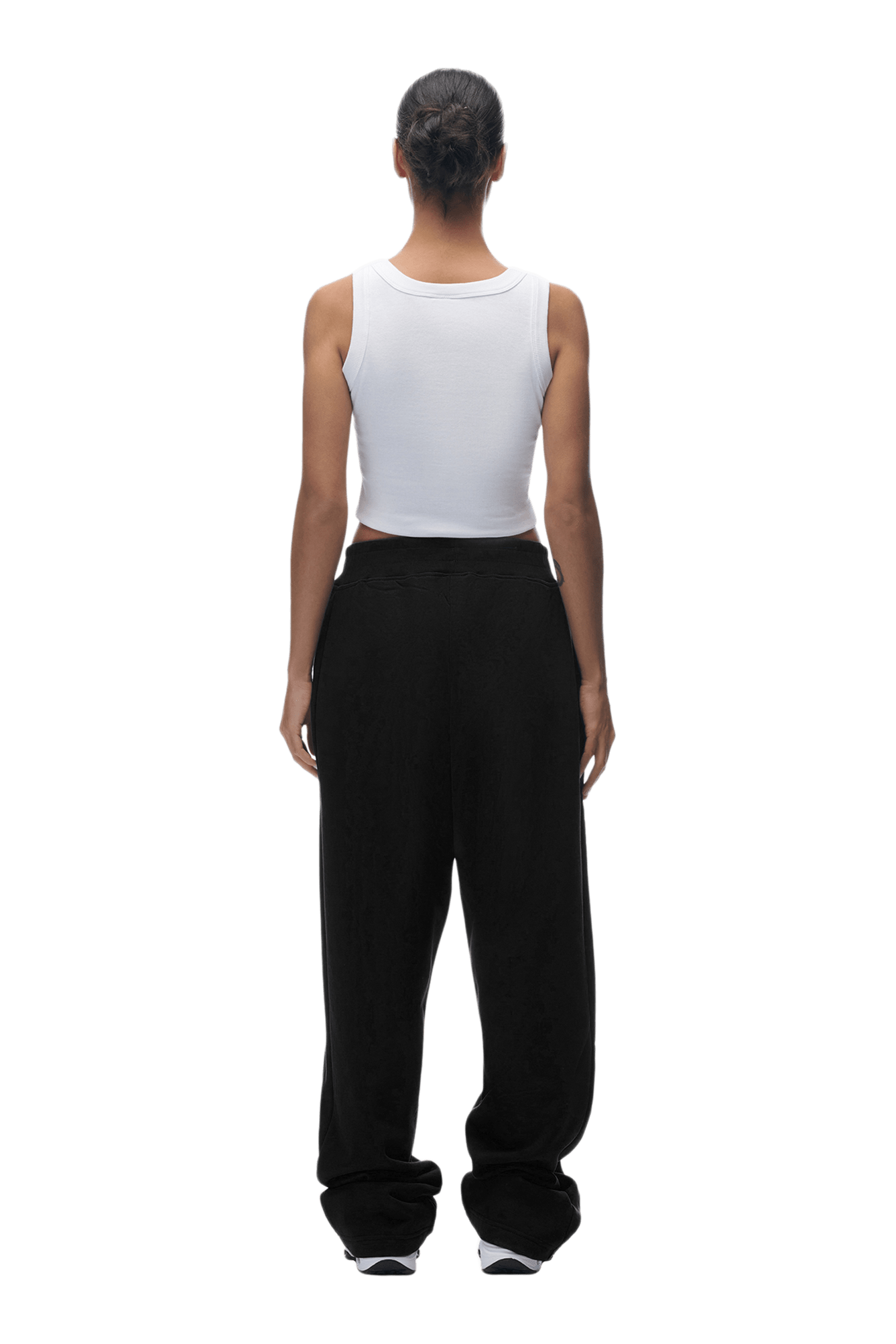 A person stands with their back to the camera, sporting a white sleeveless crop top and OPEN LEG JOGGER BLACK pants. Their hair is tied in a neat bun, and they pose against a plain green background.