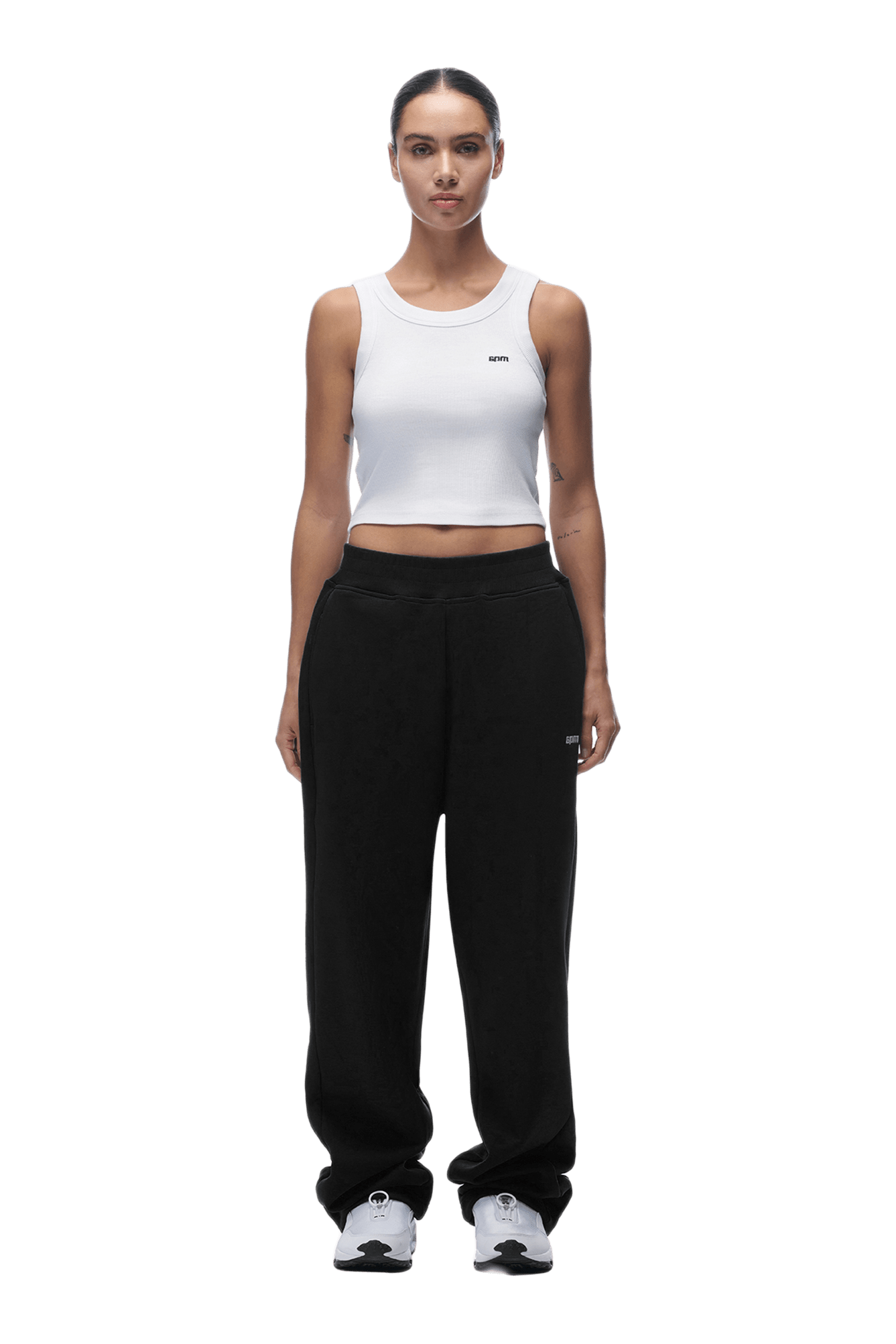 A woman faces forward, wearing a white sleeveless crop top, OPEN LEG JOGGER BLACK pants, and white sneakers. Her hair is tied back and her arms are at her sides. The background is transparent.