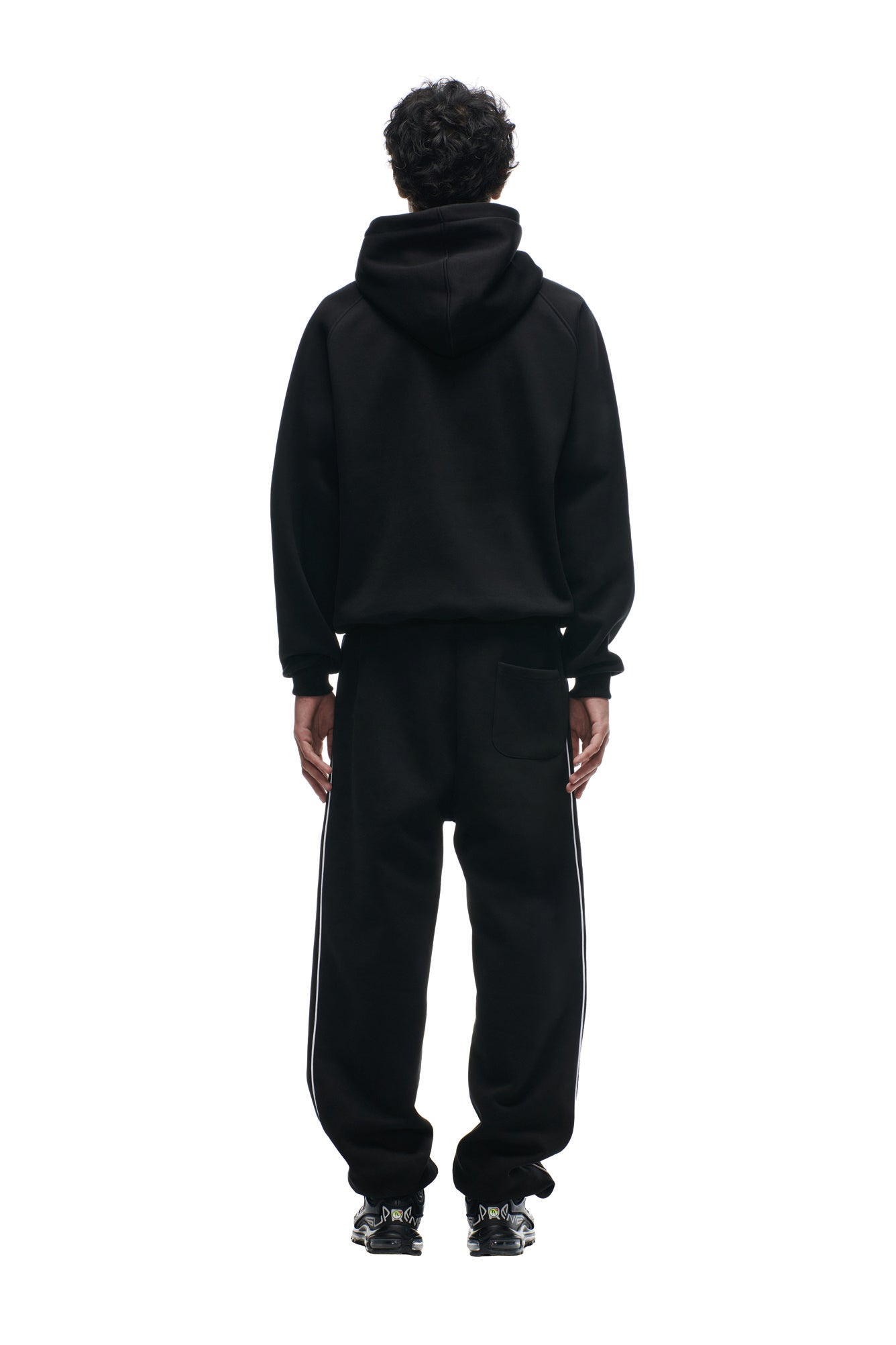 A person faces away, wearing the 6PM DOLPHINS SEASON HOODIE with matching black sweatpants featuring white side stripes and black sneakers, set against a plain white background.