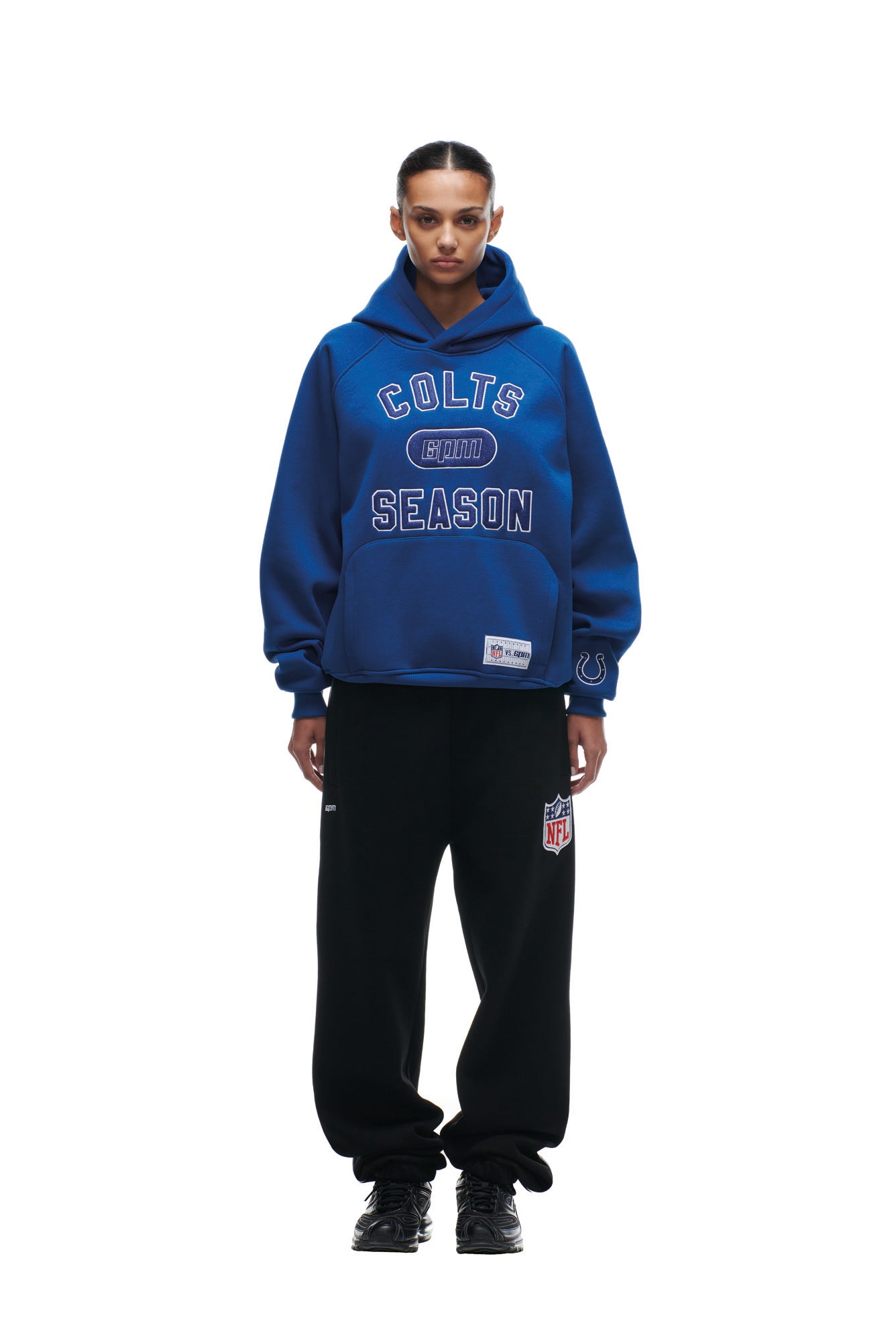 A person stands facing forward against a plain white background, wearing the 6PM COLTS SEASON HOODIE in blue and black sweatpants with an NFL logo patch.