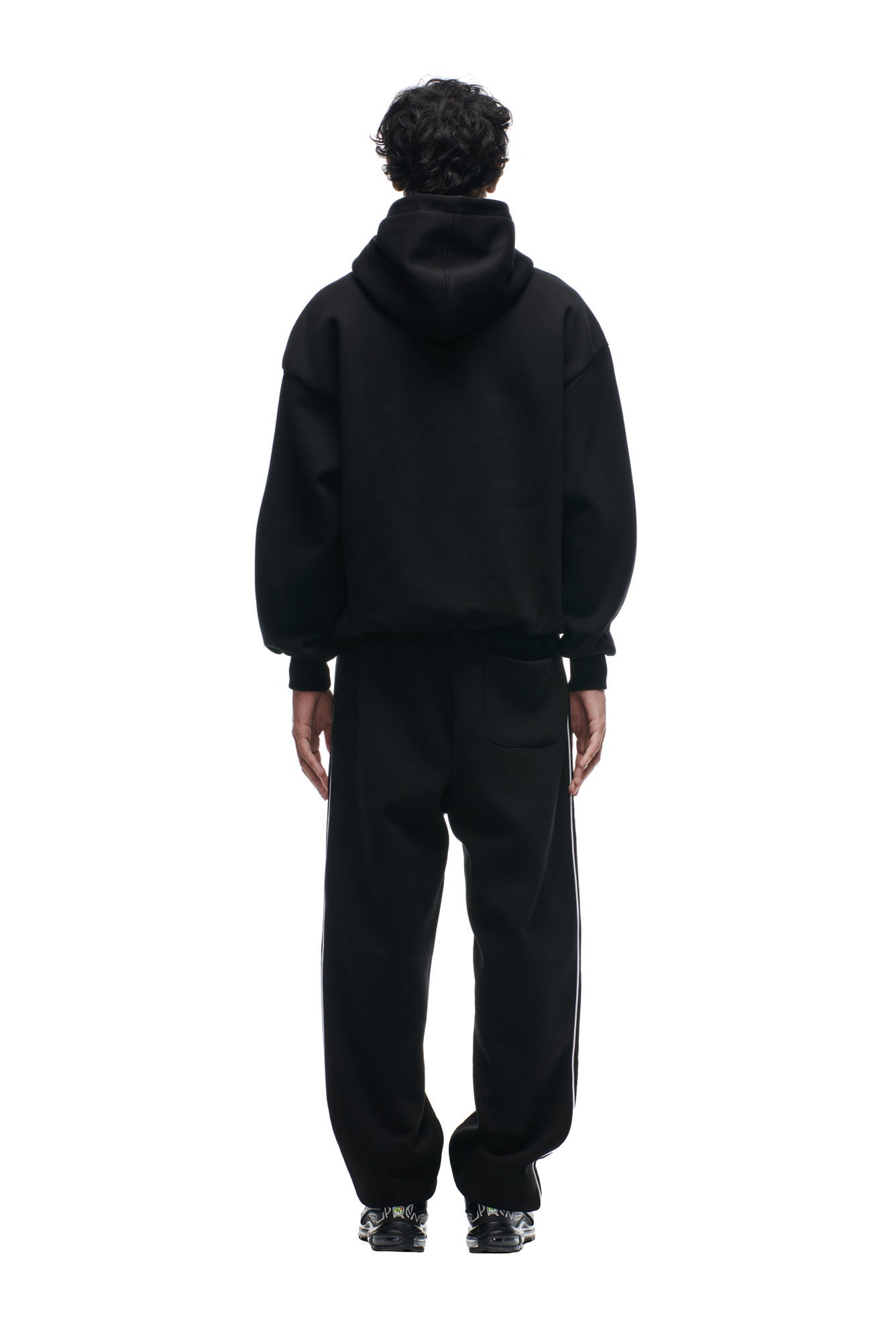 A person stands facing away from the camera, wearing the 6PM SHIELD LOGO HOODIE BLACK with black pants and sneakers, set against a plain white background.