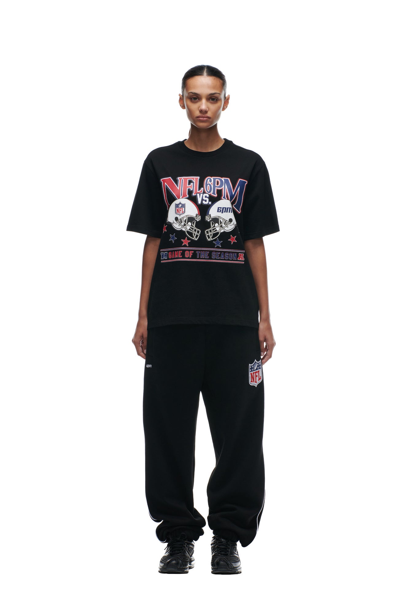 A person stands facing forward against a white background, wearing a black 6PM NFL VS 6PM T-SHIRT and matching black sweatpants with NFL logos, paired with black sneakers.
