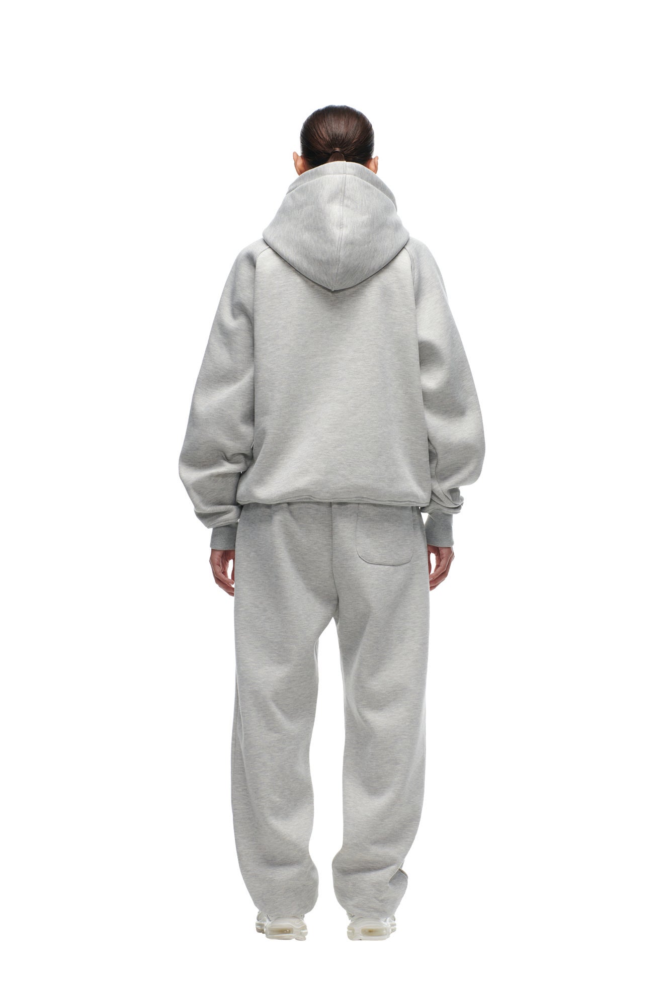 A person stands facing away on a white background, wearing the 6PM CHIEFS SEASON HOODIE in light gray with the hood up and matching sweatpants. Their hands rest relaxed at their sides.