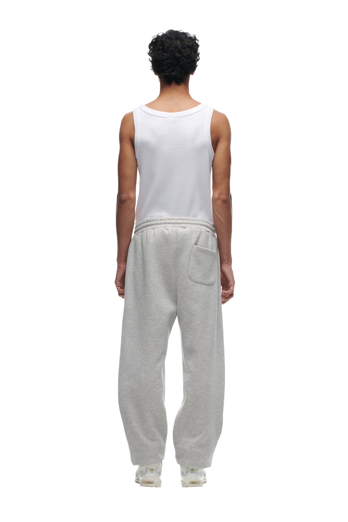 A person with short curly hair faces away, wearing a white sleeveless tank top, white sneakers, and 6PM CHIEFS SEASON JOGGER sweatpants against a plain white background.