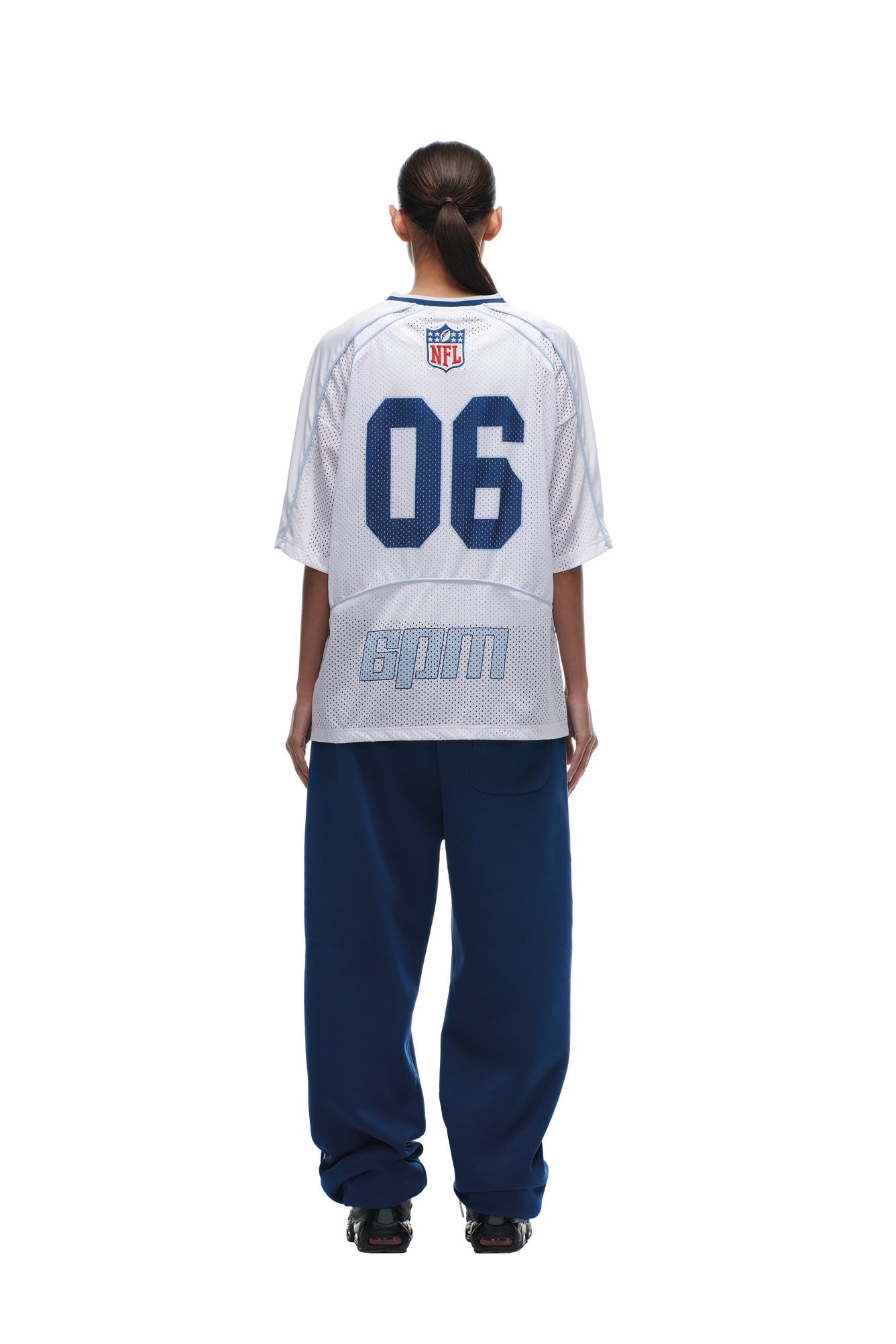 A person stands facing away against a plain white background, wearing the 6PM NFL MESH SHIRT paired with loose blue pants and black shoes.