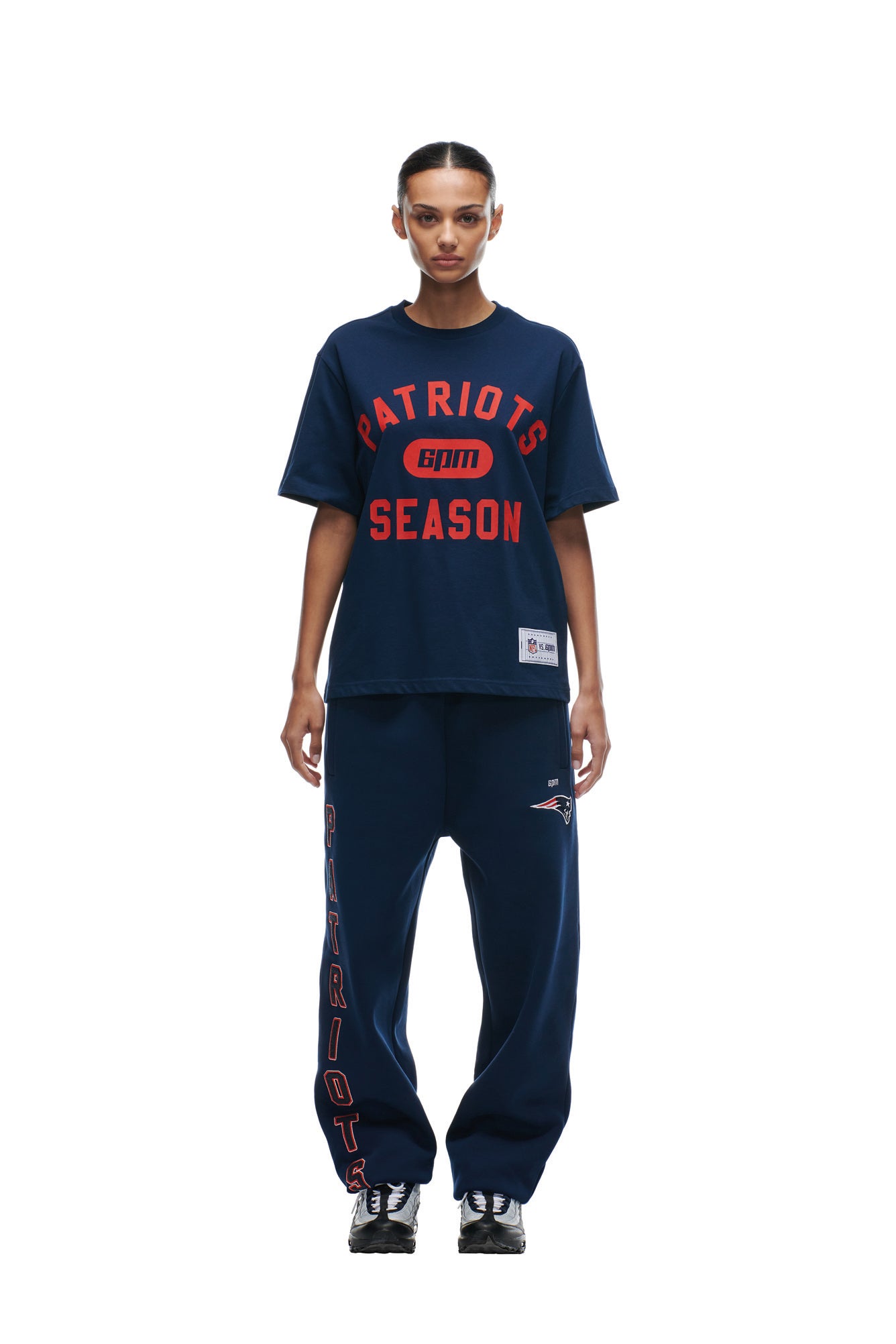 A person faces forward in a 6PM PATRIOTS SEASON T-SHIRT in navy blue, matched with navy sweatpants featuring "PATRIOTS" and logo down the side, plus black sneakers, all shown against a white background.