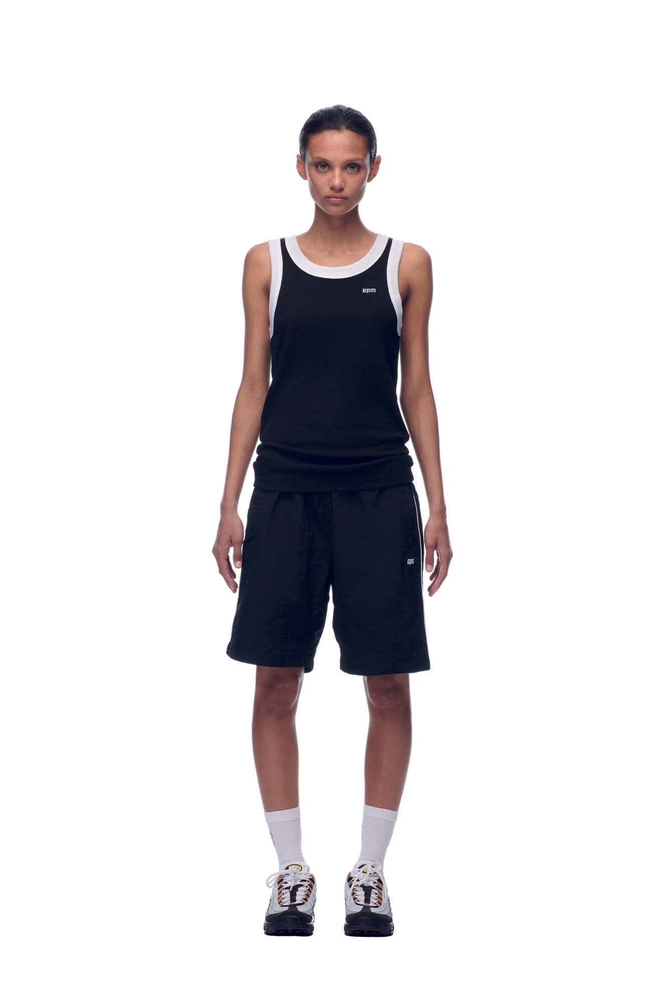 A person faces forward against a white background, wearing the 6PM NH TANKTOP BLACK/WHITE, loose black shorts, white crew socks, and black-and-white sneakers.