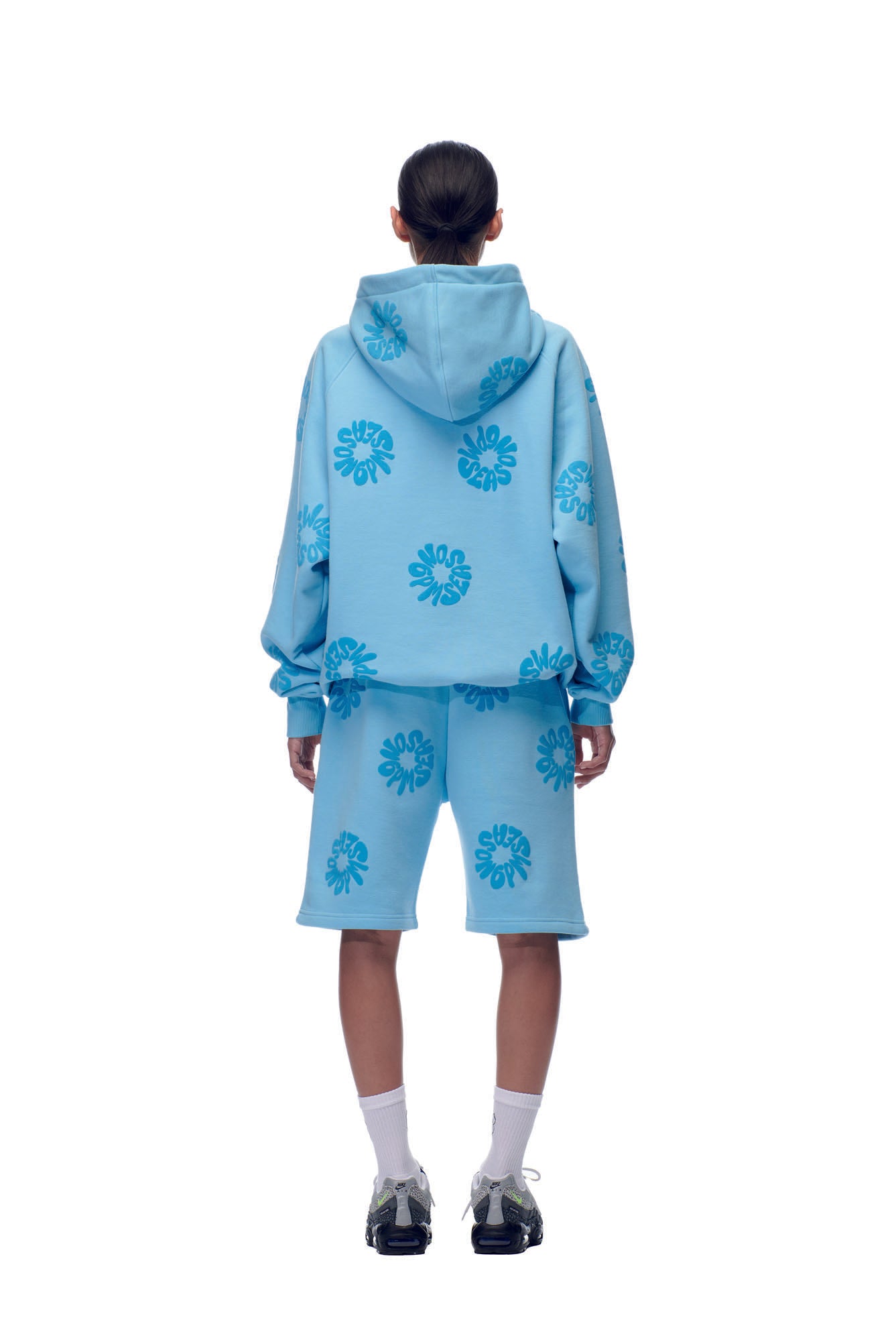 A person faces away, wearing the 6PM FLOWER HOODIE BABY BLUE and matching shorts with dark blue graphics, paired with white socks and black sneakers, set against a plain white background.