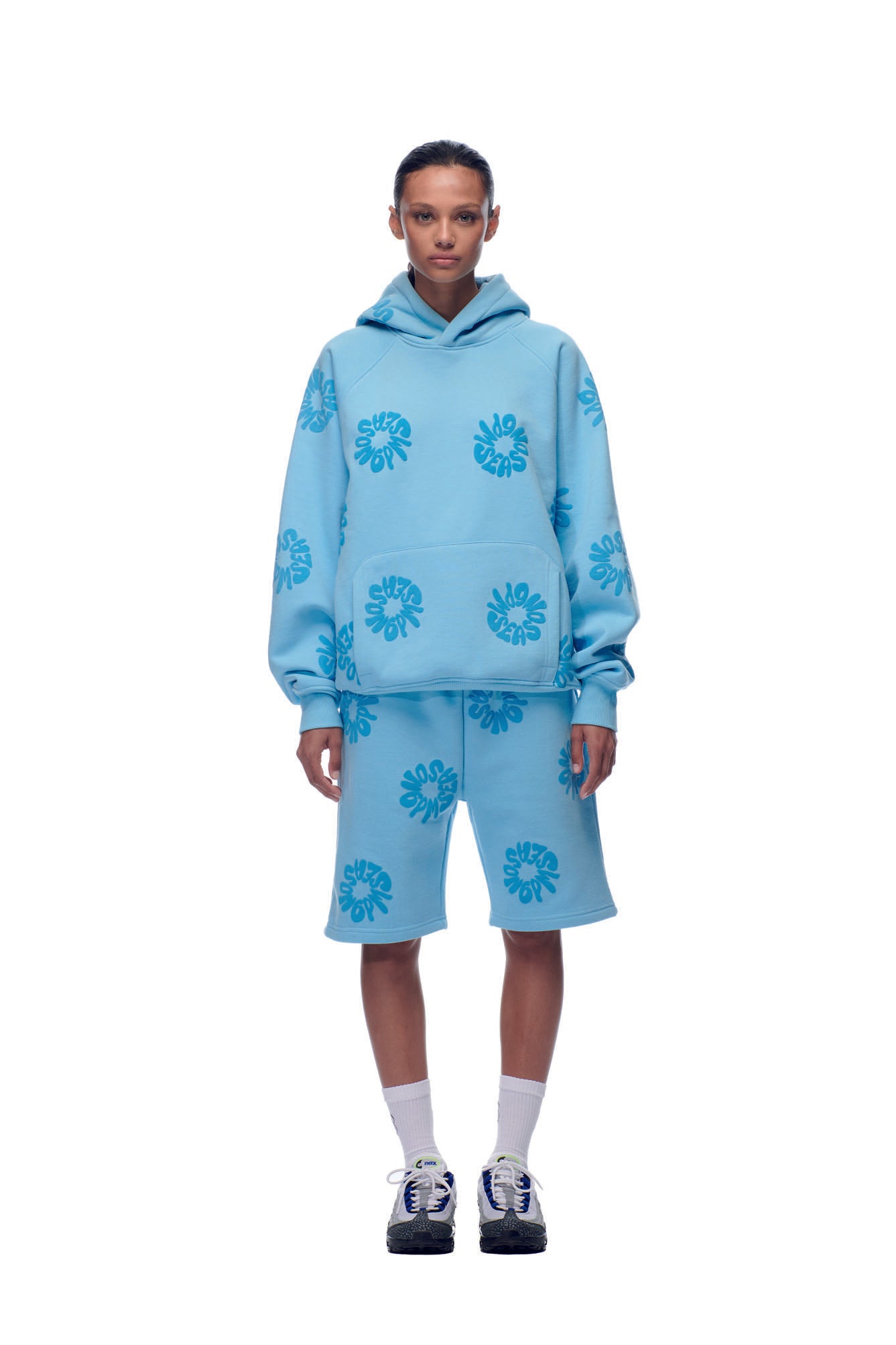 A person stands against a white background wearing the 6PM FLOWER HOODIE BABY BLUE with matching shorts, white socks, and black sneakers.
