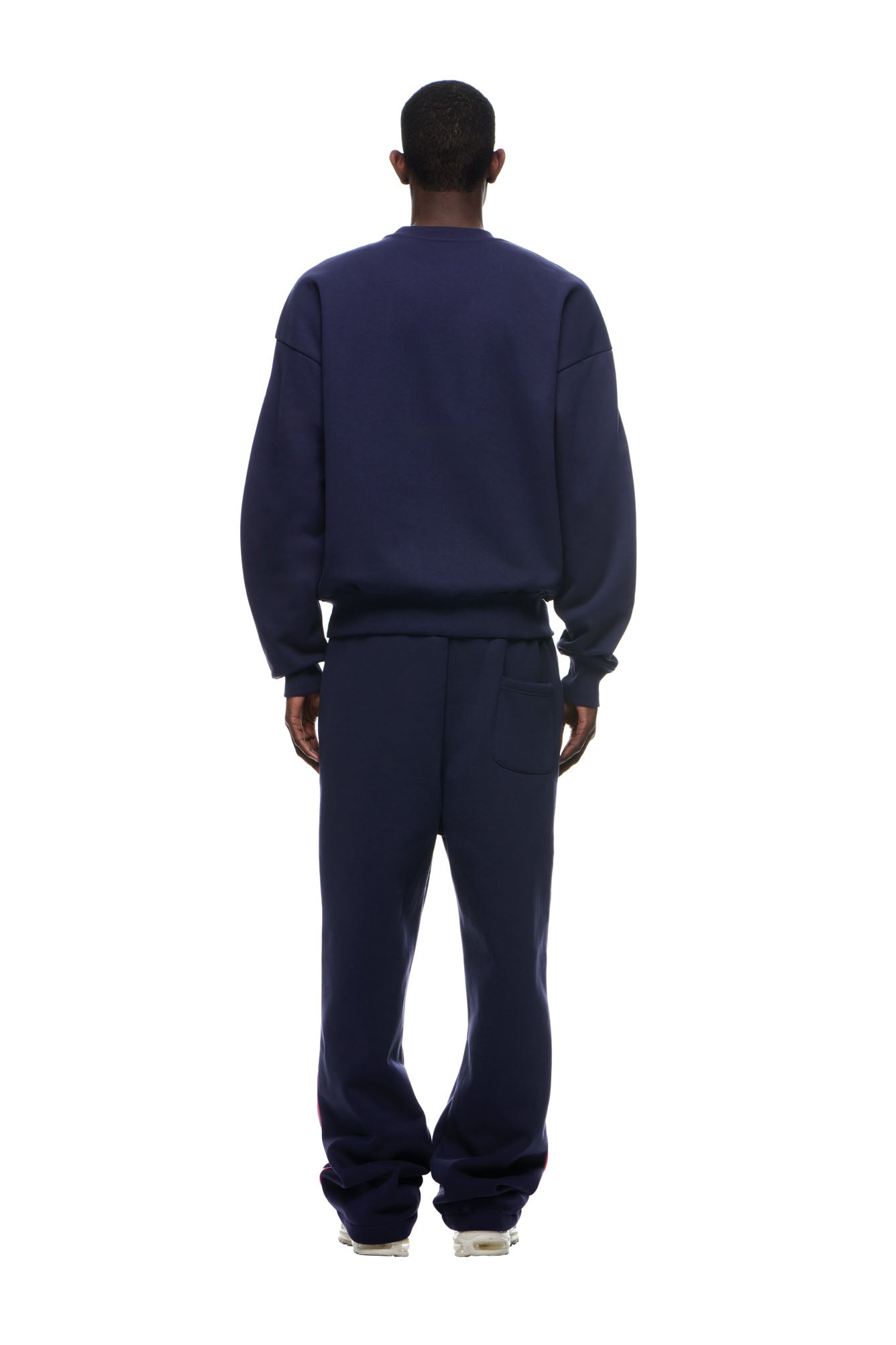 A person stands with their back to the camera, wearing the 6PM RECORDS CREWNECK DEEP BLUE sweatshirt and sweatpants with white sneakers, set against a plain white background.
