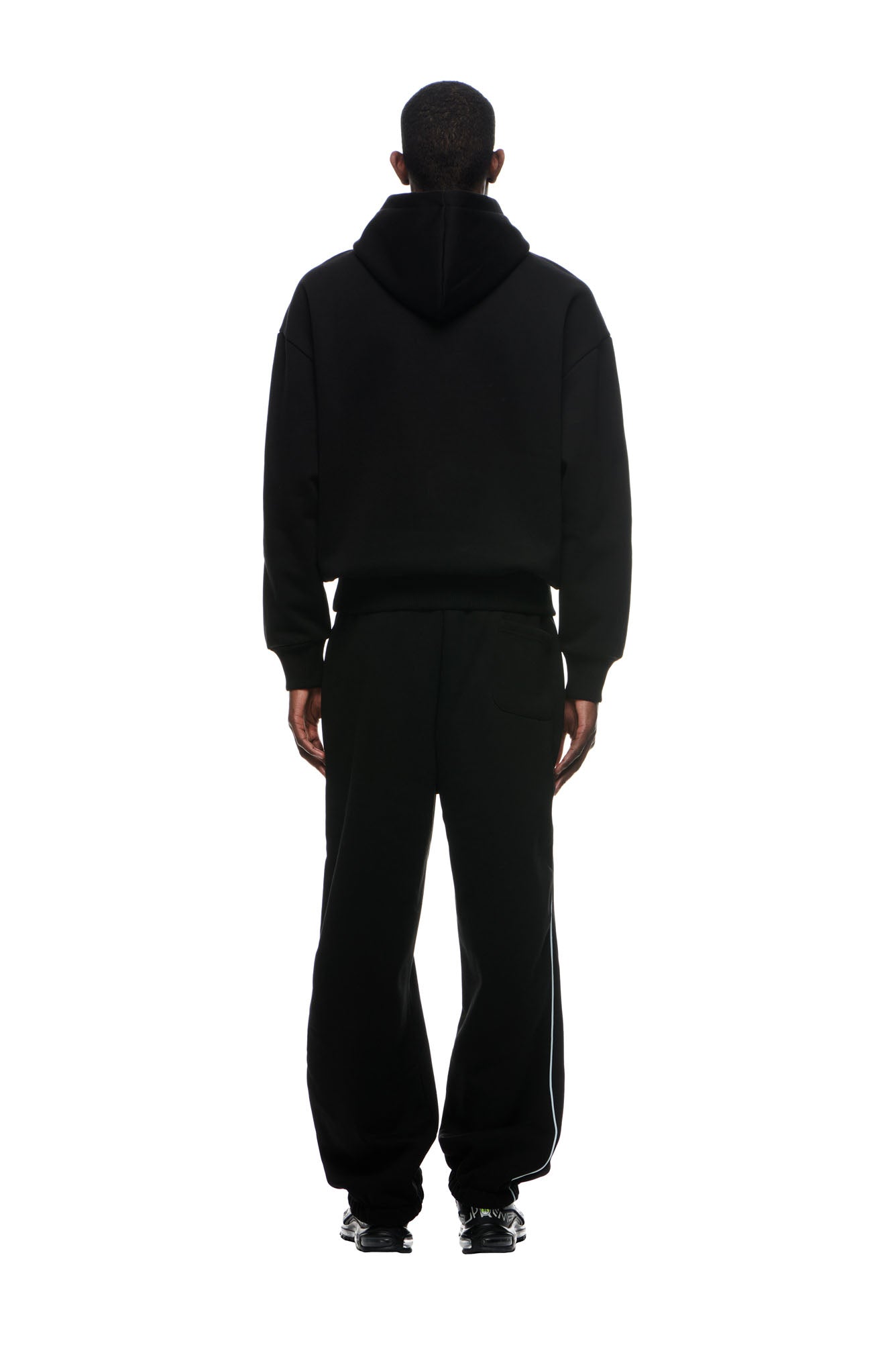 A person stands with their back to the camera, wearing the 6PM RECORDS HOODIE BLACK along with black sweatpants and black sneakers, set against a white background.