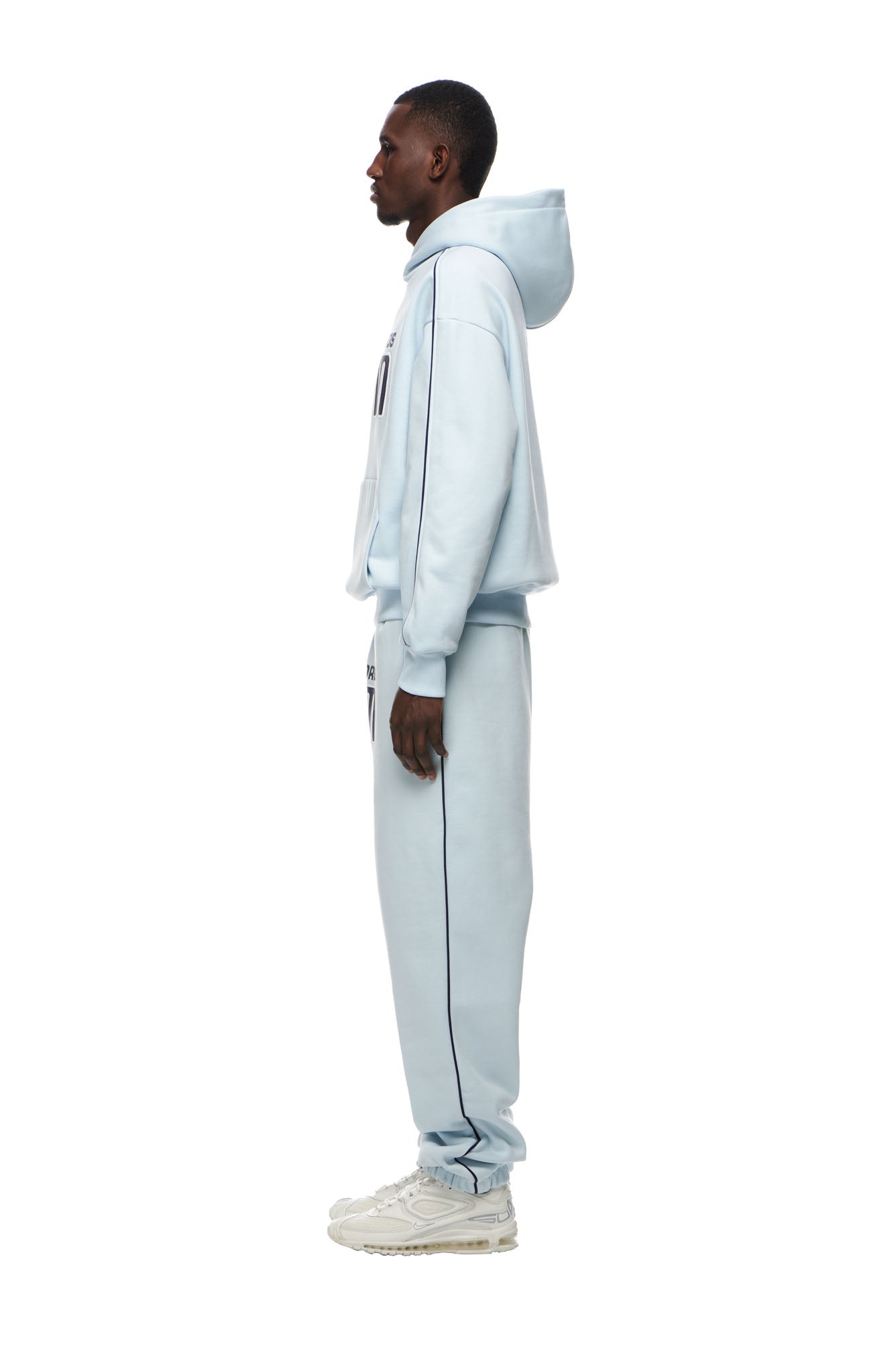 A man stands in profile wearing the 6PM RECORDS HOODIE ICE BLUE with matching sweatpants and white sneakers, set against a plain white background.