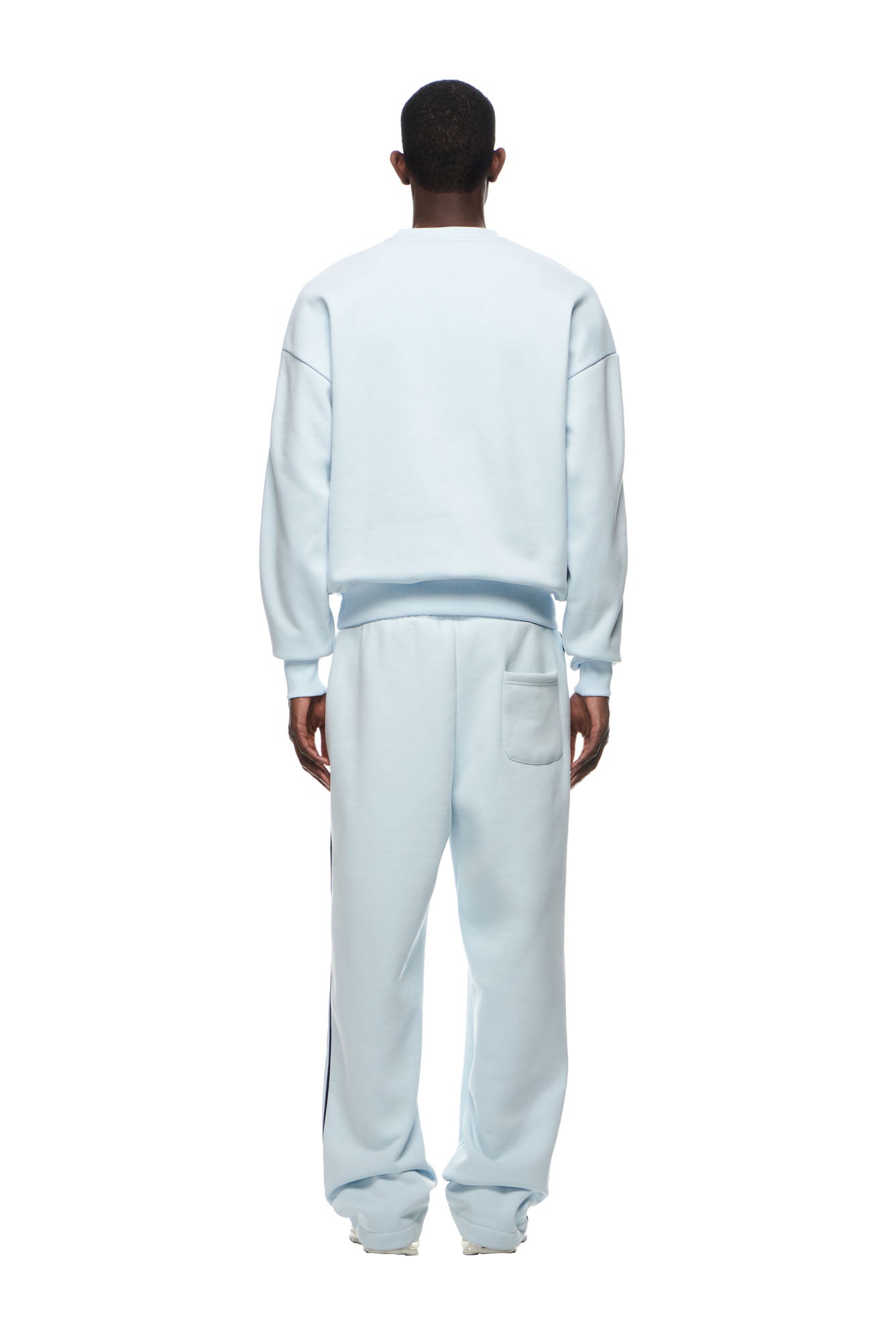 A person faces away from the camera, wearing the 6PM RECORDS CREWNECK ICE BLUE sweatshirt and matching pants with a back pocket. The background is plain white.