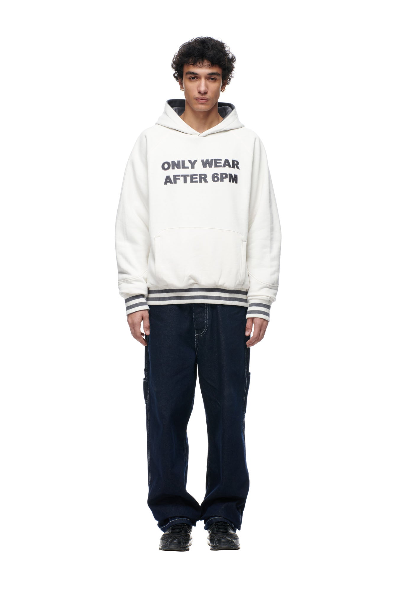 A person stands facing forward against a plain white background, wearing 6PM's ONLY WEAR REVERSIBLE HOODIE in anthracite/cream, dark baggy jeans, and black shoes.