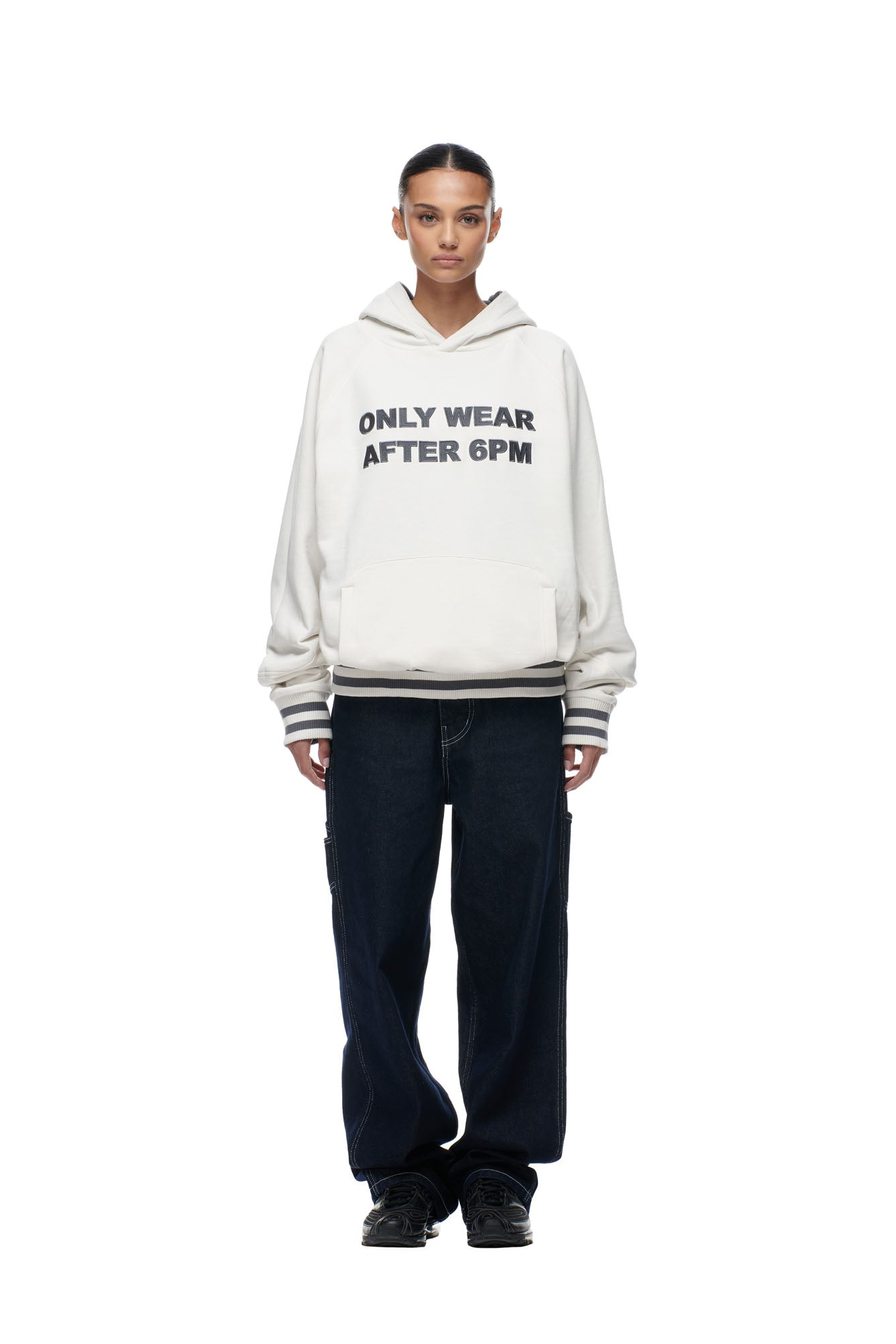A person stands forward against a plain white background, wearing the 6PM ONLY WEAR REVERSIBLE HOODIE in anthracite/cream, paired with dark loose-fitting jeans and black sneakers.