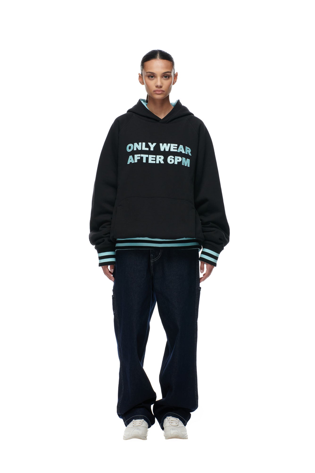 A person stands facing forward in a 6PM ONLY WEAR REVERSIBLE HOODIE BLACK/TURQUOISE, loose dark jeans, and white sneakers, set against a plain white background.