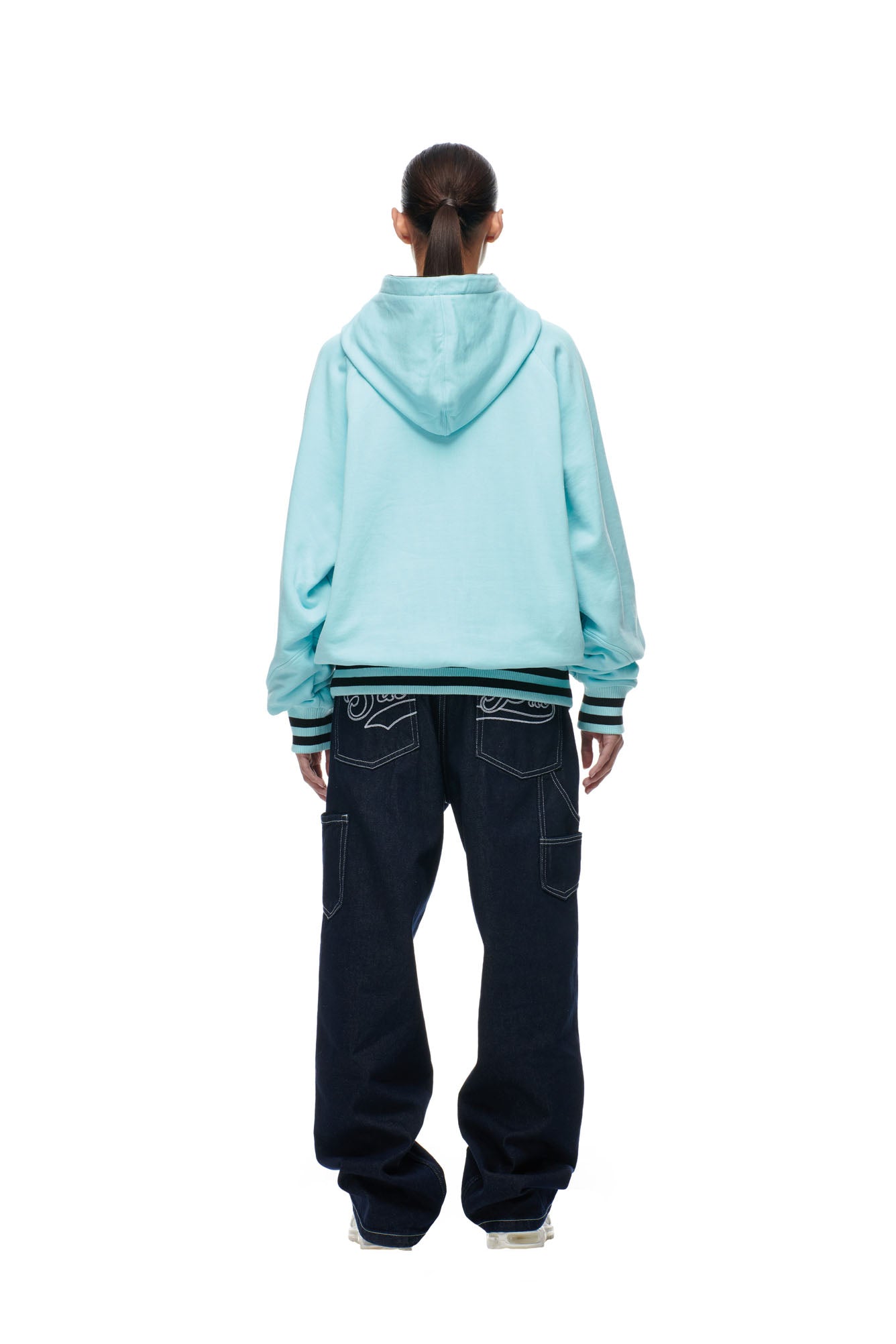 Person stands with their back to the camera, wearing the 6PM ONLY WEAR REVERSIBLE HOODIE in black/turquoise, paired with dark baggy jeans and white sneakers against a plain white background.