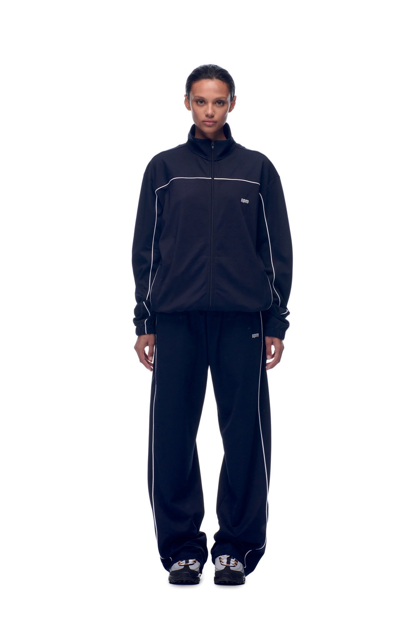 A person stands facing forward, wearing the 6PM TENNIS TRAINER JACKET BLUE with matching sneakers, against a plain white background.