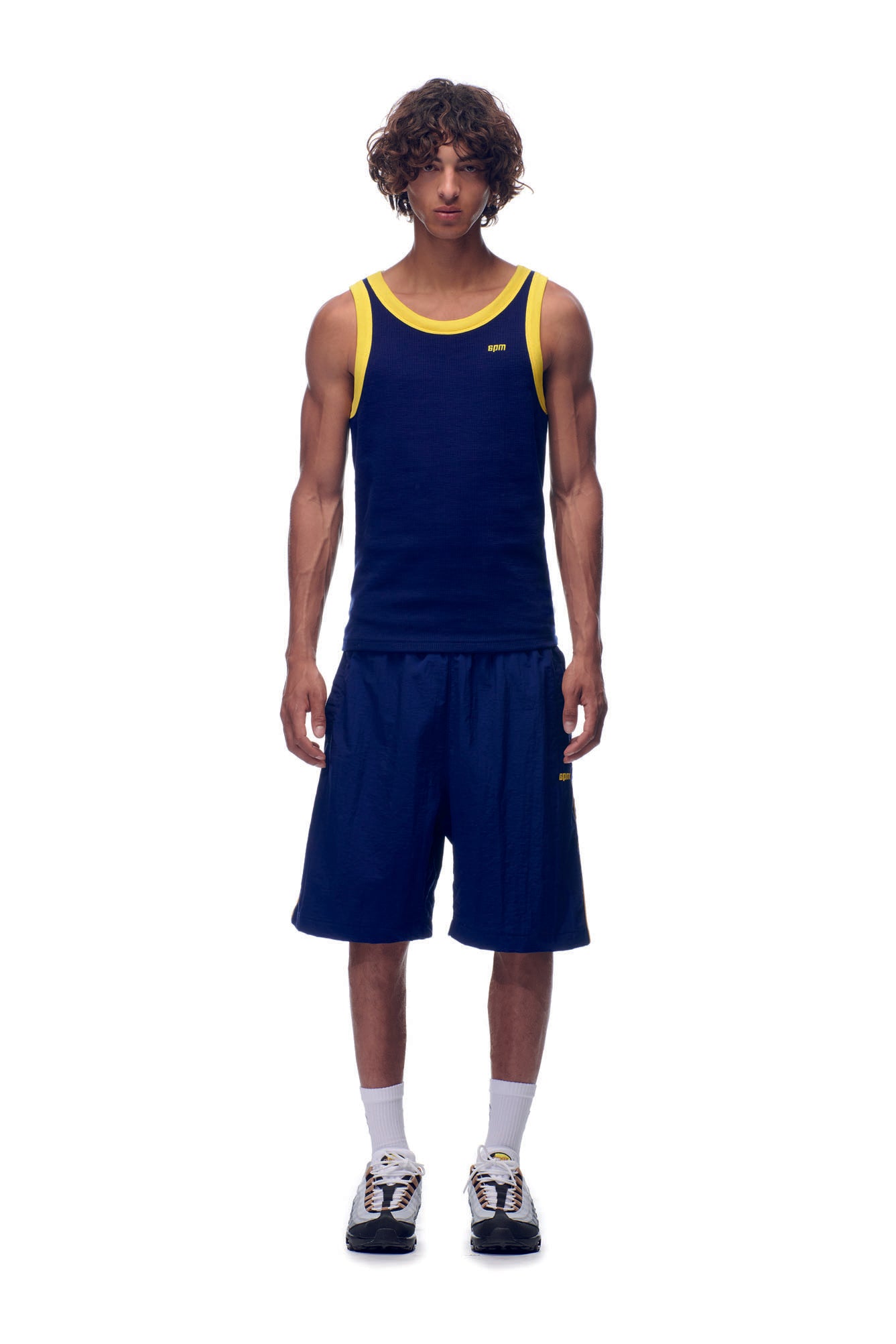 A young man stands facing forward in a 6PM NH TANKTOP NAVY/YELLOW, paired with matching navy shorts, white socks, and sneakers against a plain white background.