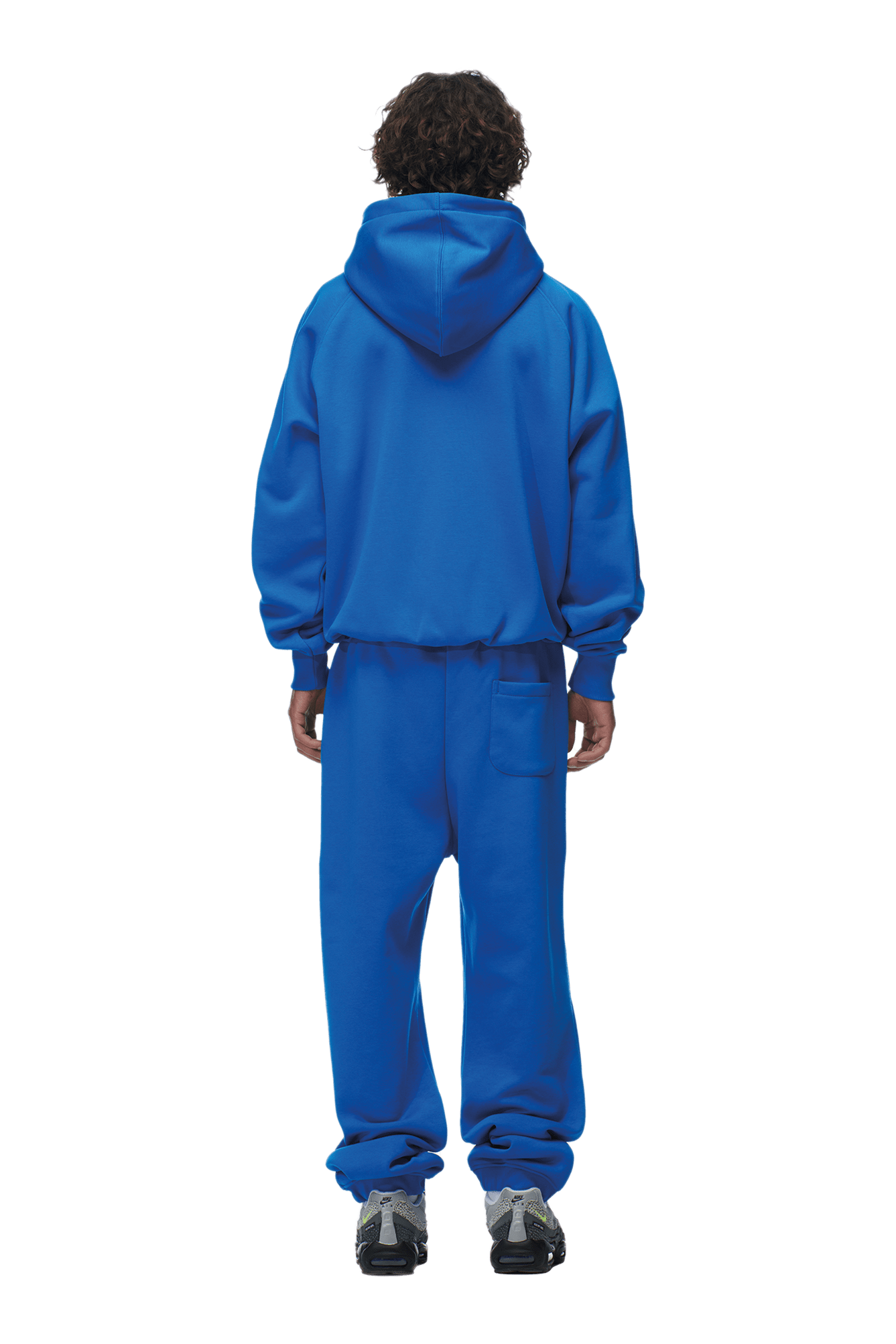 A person stands with their back to the camera, wearing the 6PM ZIP HOODIE PRINCESS BLUE and matching sweatpants, paired with gray and black sneakers. The clean look is ideal for everyday wear. Background is transparent.