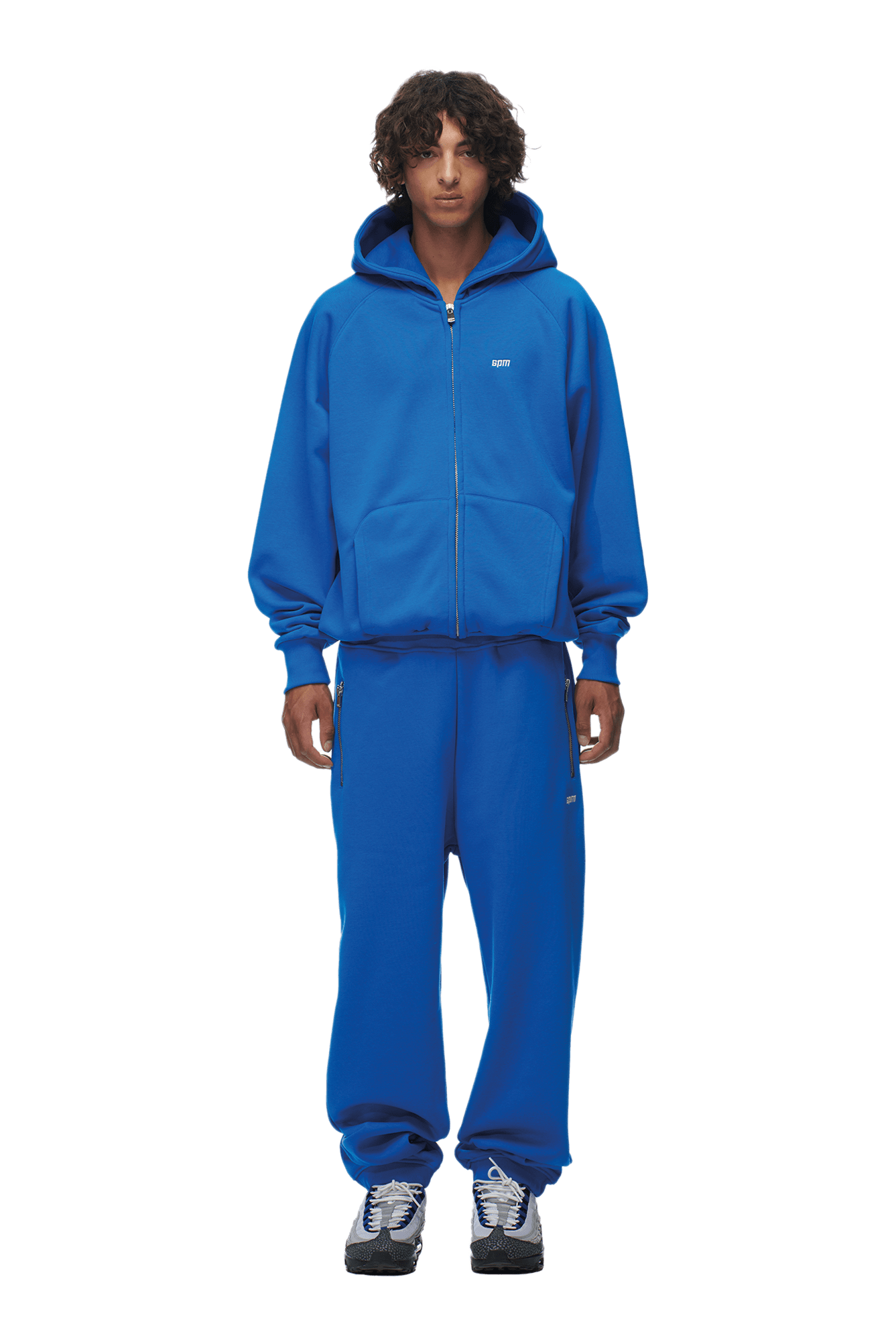 A person faces forward in the 6PM ZIP HOODIE PRINCESS BLUE with the hood up, paired with matching blue sweatpants and black-and-white sneakers. The look is clean and ideal for daily wear. Background is transparent.