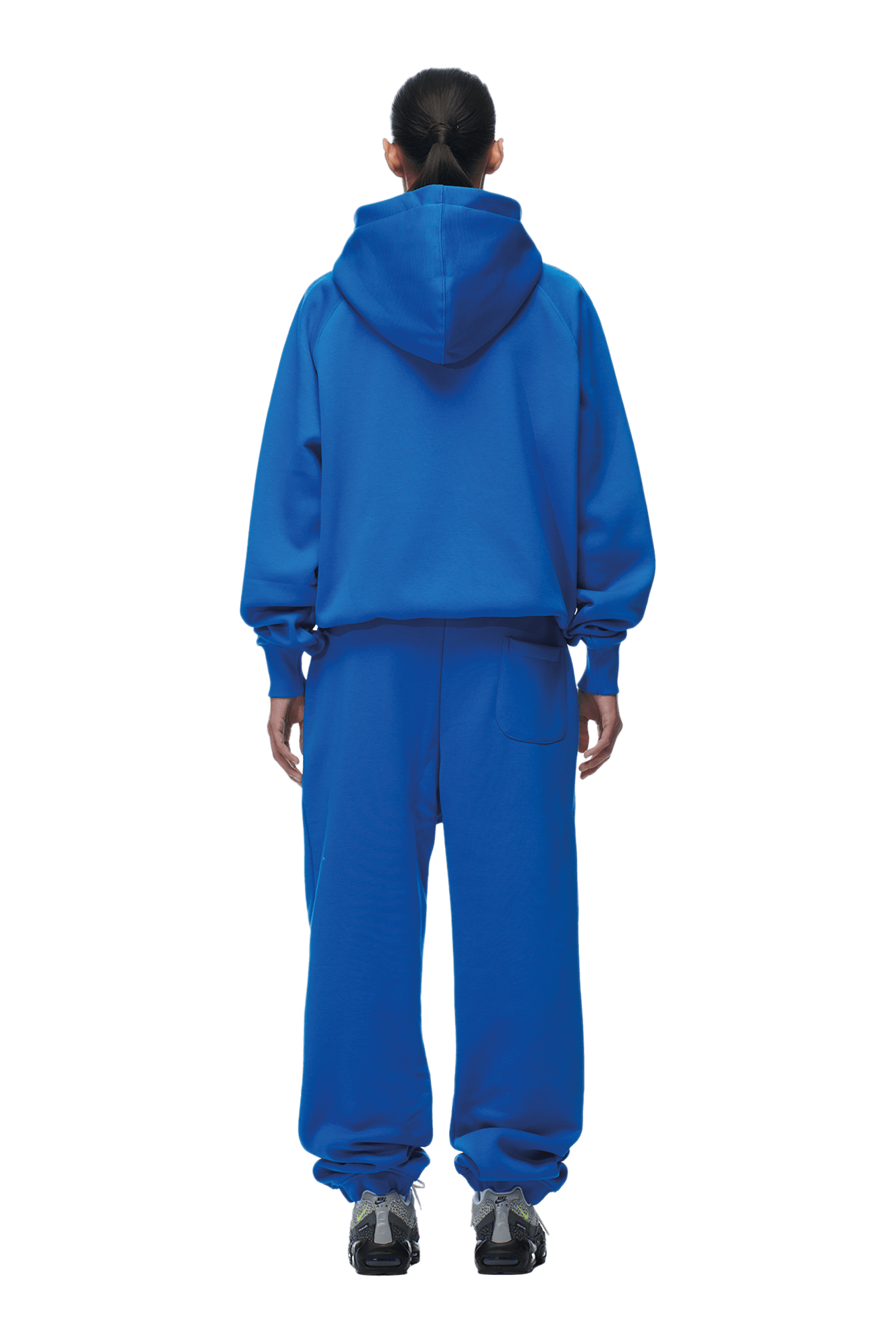 A person stands facing away in a 6PM ZIP HOODIE PRINCESS BLUE and matching sweatpants with black sneakers, hair tied back. The outfit’s structured, clean finish makes it perfect for daily wear. Background is transparent.