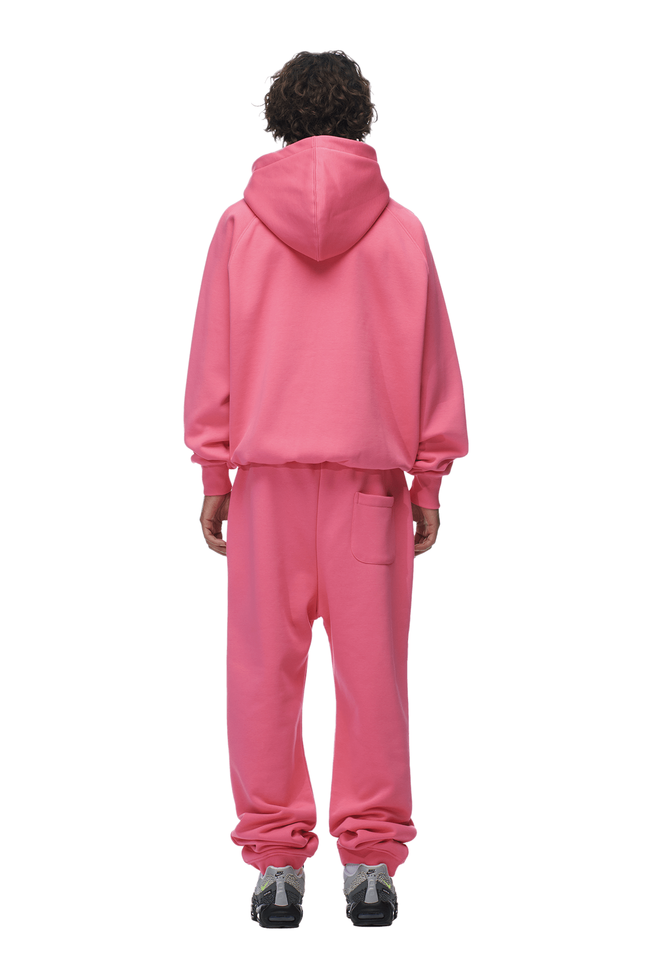 A person with curly hair faces away, wearing the 6PM ZIP HOODIE HOT PINK and matching sweatpants with gray sneakers. The outfit’s clean finish is perfect for daily wear. Background is transparent.