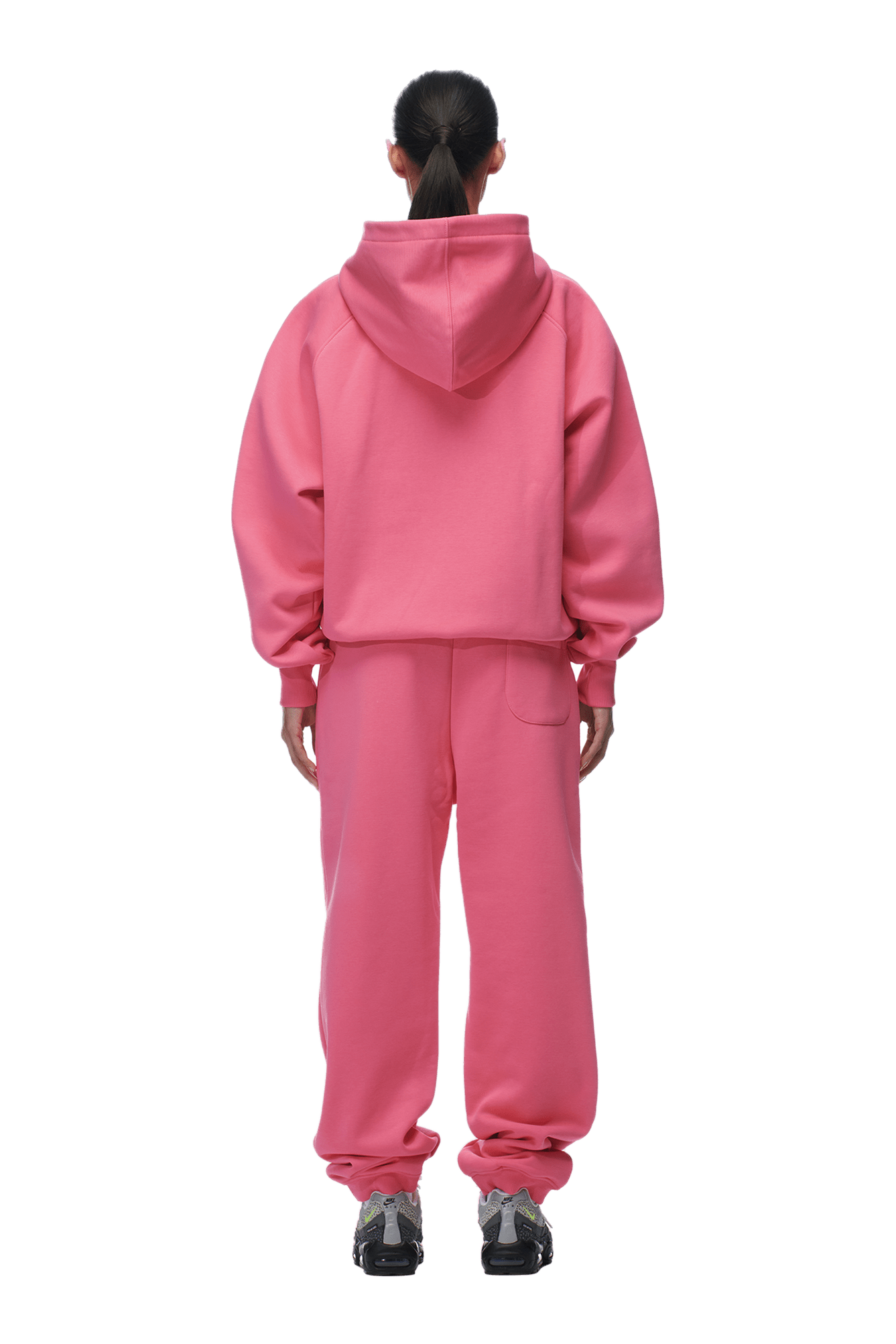 A person with a ponytail faces away from the camera, wearing the 6PM ZIP HOODIE HOT PINK and matching sweatpants, paired with black and gray sneakers. The background is transparent.