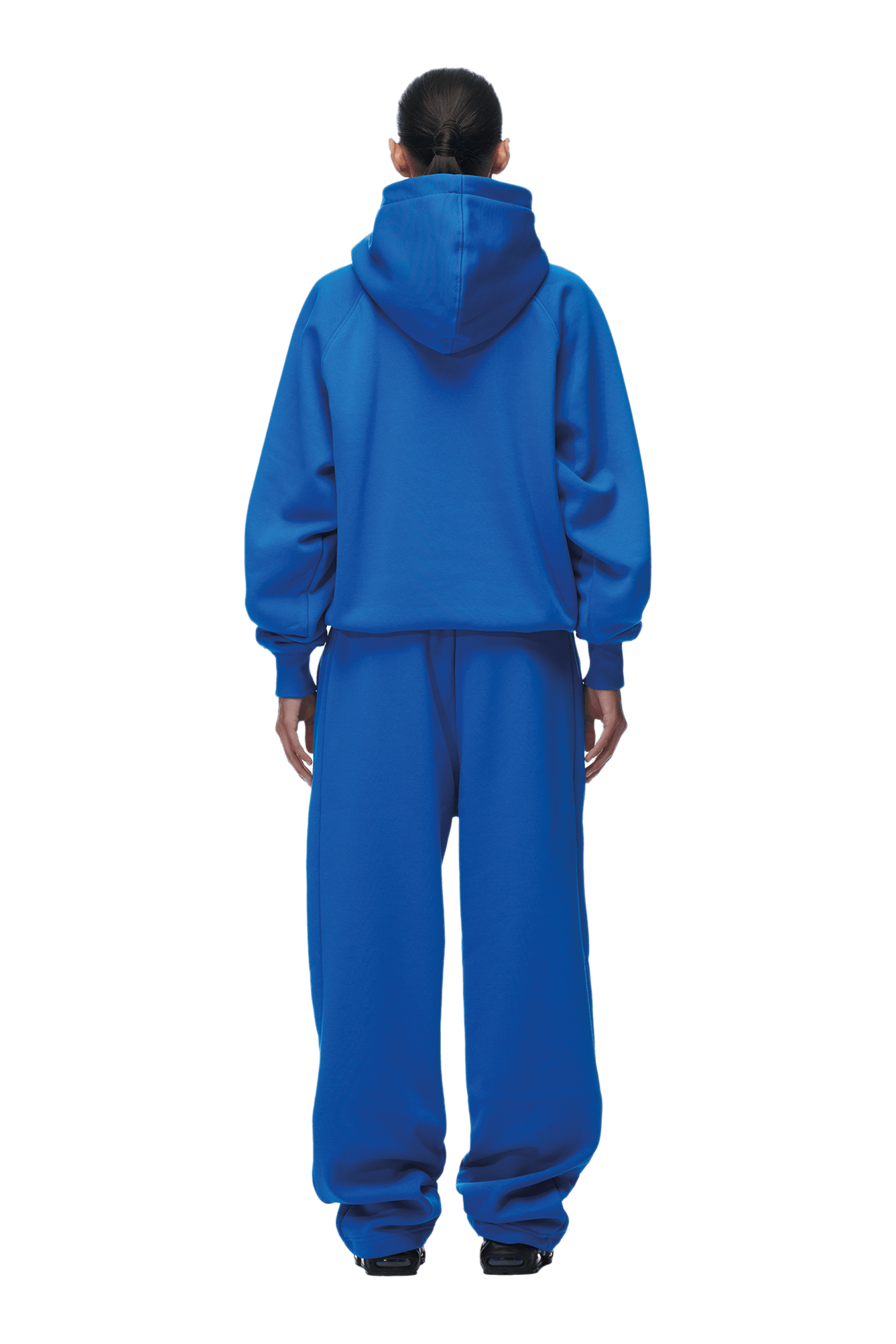 A person with their back to the camera wears the 6PM HOODIE PRINCESS BLUE—a loose-fit blue raglan sleeve hoodie with kangaroo pocket—paired with matching sweatpants and black shoes. Their hair is tied back; background is transparent.