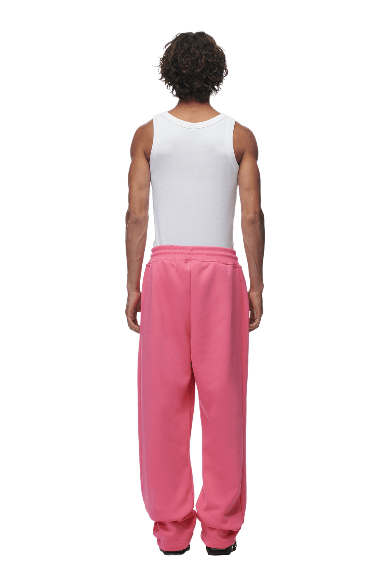 A person with curly hair stands facing away, wearing a white tank top and 6PMs OPEN LEG JOGGER HOT PINK sweatpants, featuring a modern classic open-leg design with the perfect stacking length against a plain background.