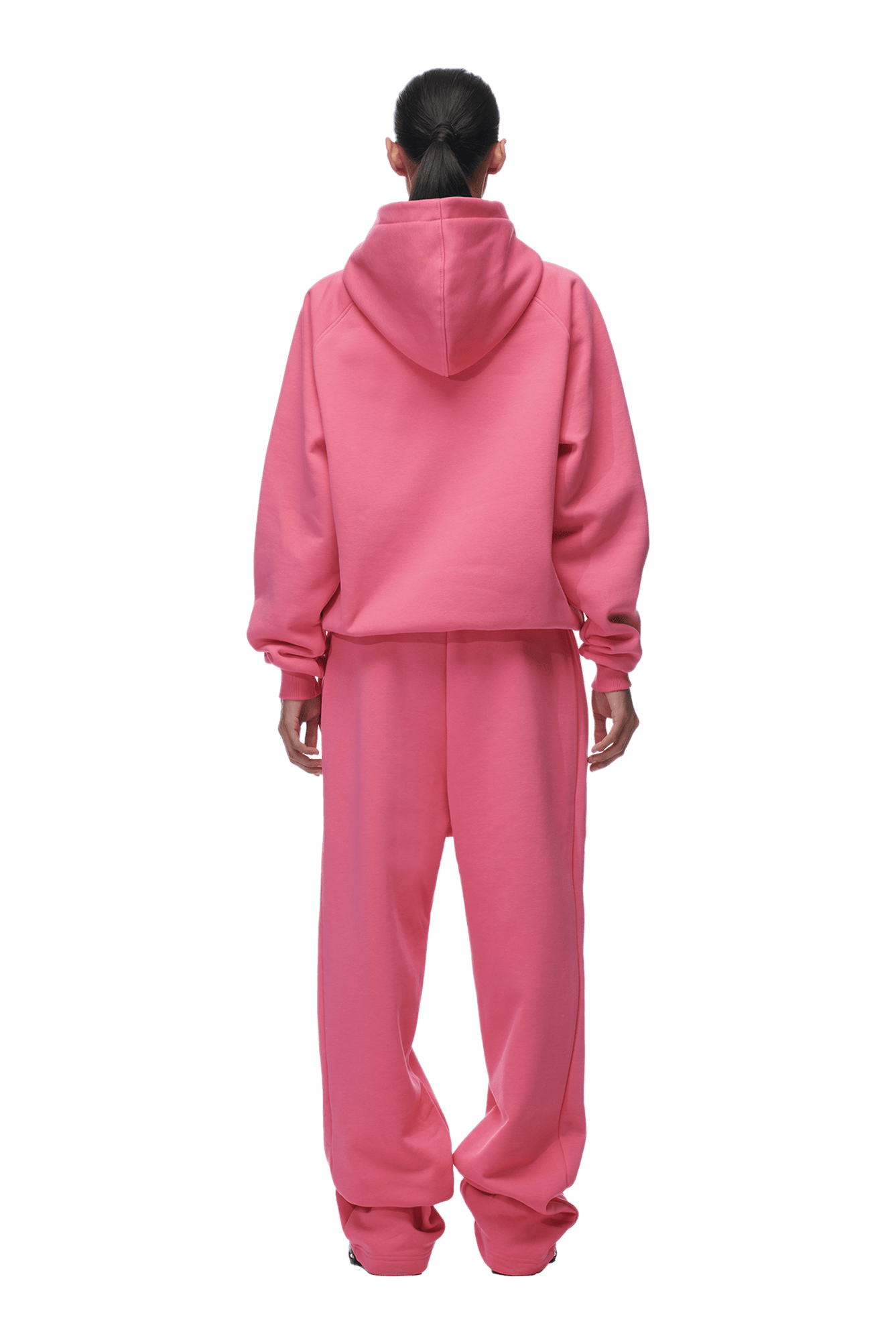 A person with dark hair in a low ponytail wears the 6PM HOODIE HOT PINK, a loose-fitting raglan-sleeved hoodie with kangaroo pocket and matching sweatpants. They are facing away and the background is transparent.