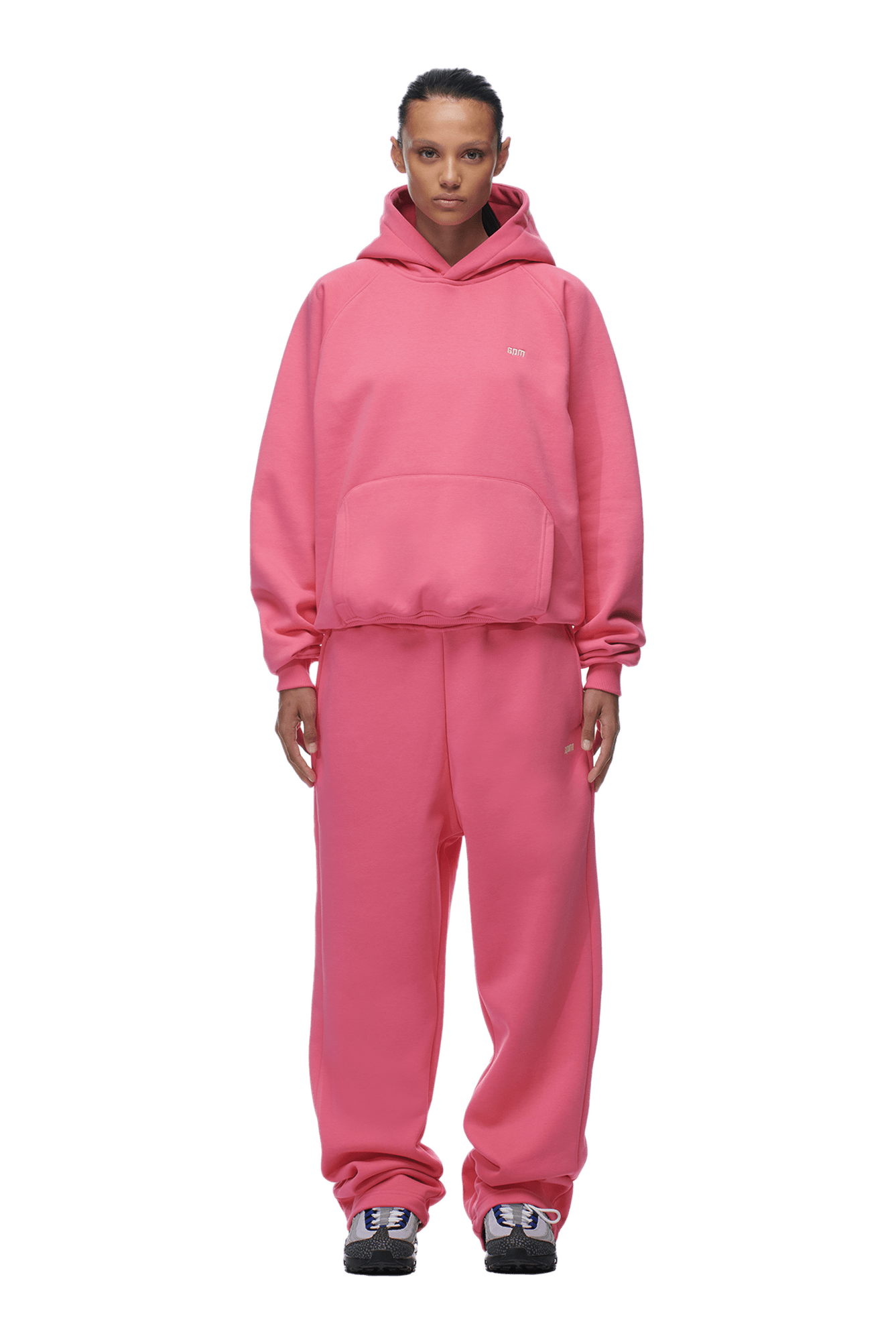 A person faces forward, wearing a 6PM HOODIE HOT PINK with raglan sleeves and kangaroo pocket, paired with matching pink sweatpants and black-and-white sneakers, perfect for everyday wear, set against a plain green background.