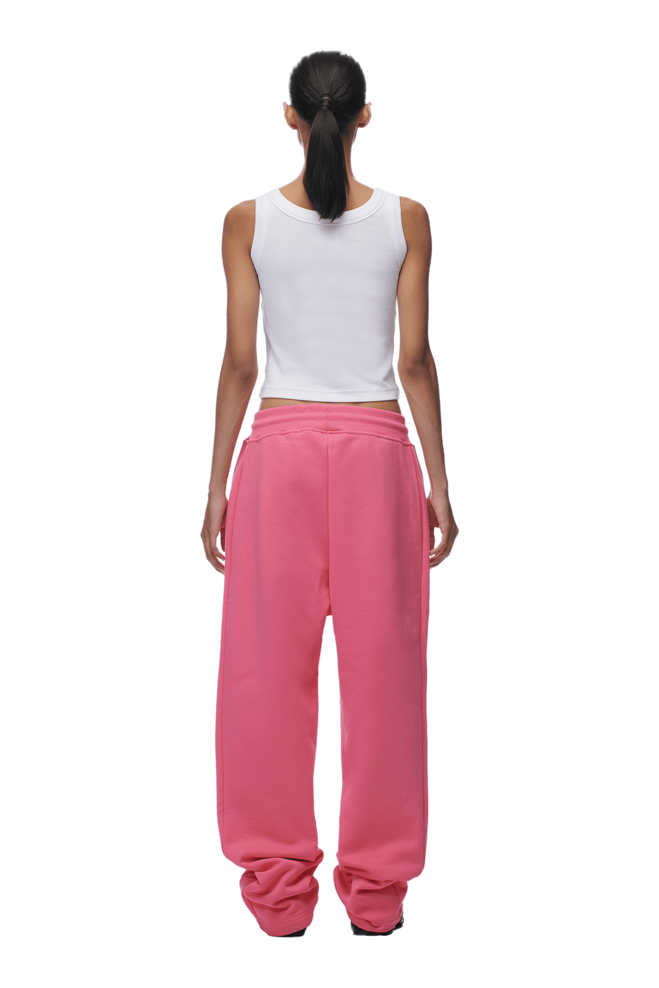 A person with long dark hair in a ponytail stands facing away from the camera, wearing a white sleeveless top and 6PMs OPEN LEG JOGGER HOT PINK pants against a plain background.