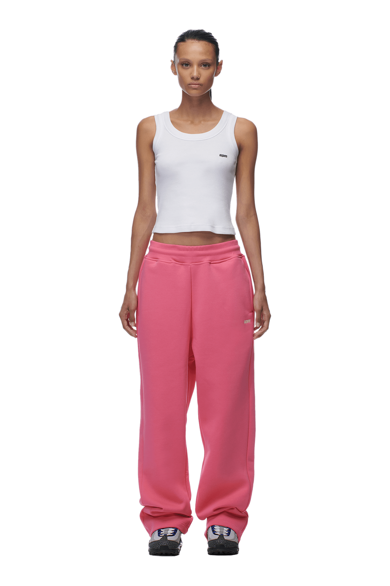 A woman faces forward against a plain green background, wearing 6PMs OPEN LEG JOGGER HOT PINK sweatpants, a fitted white tank top, and black sneakers.
