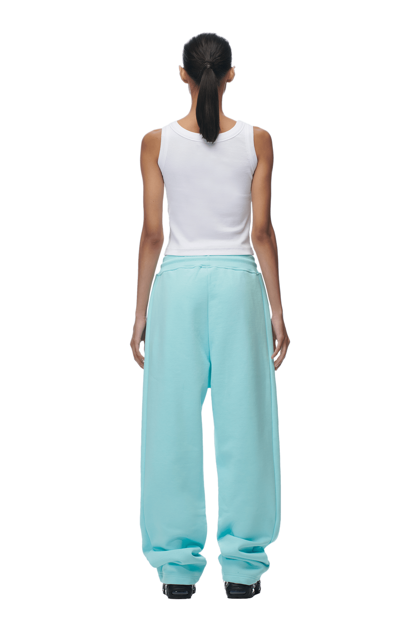 A person with long dark hair in a ponytail wears a white sleeveless top and 6PM’s OPEN LEG JOGGER TURQUOISE pants, standing with their back to the camera against a plain background for a modern classic look.